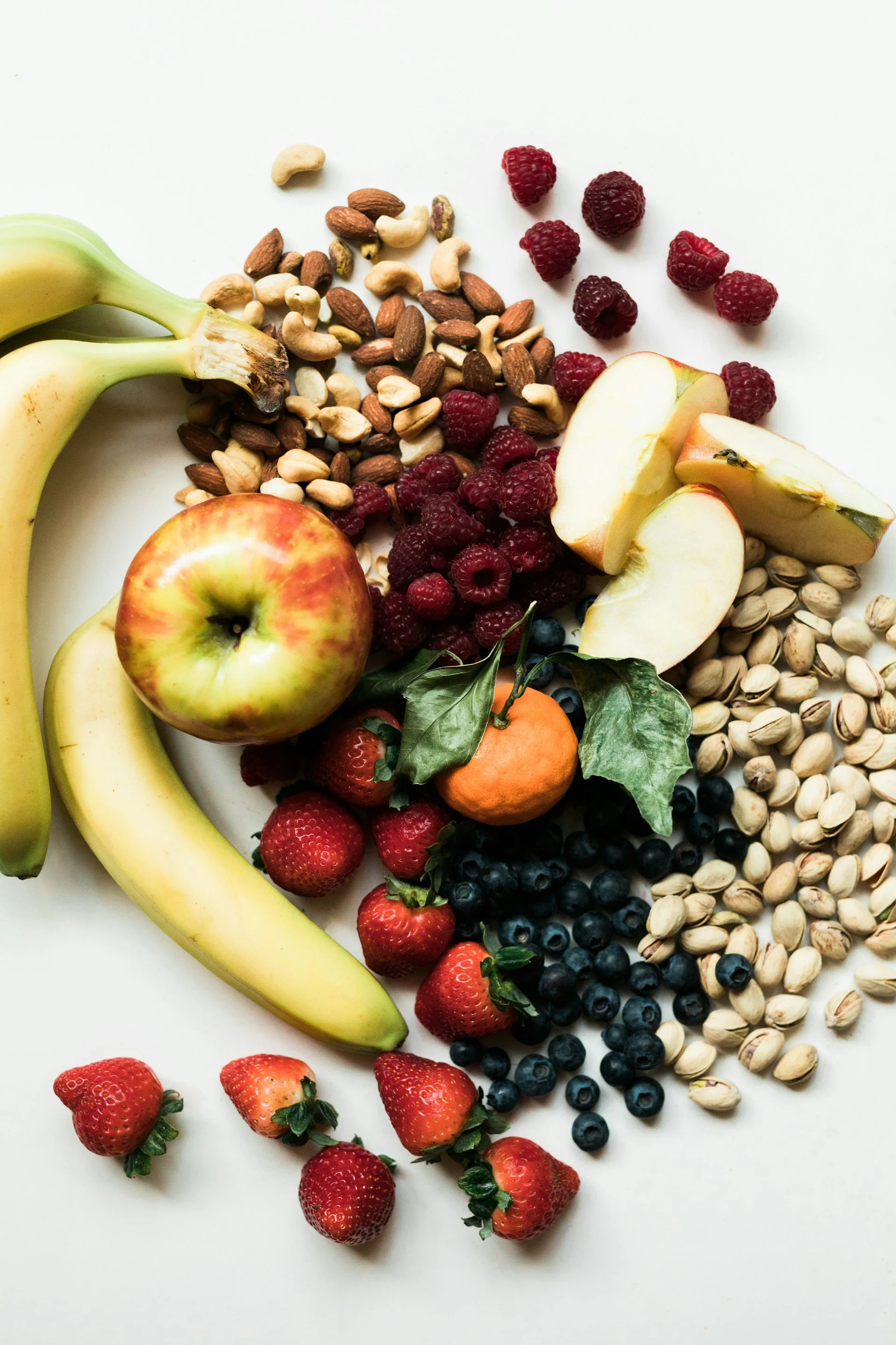Sélection de bananes, pommes, mandarines, fraises, framboises, pistaches et oléagineux pour illustrer une alimentation variée favorable au microbiote intestinal.