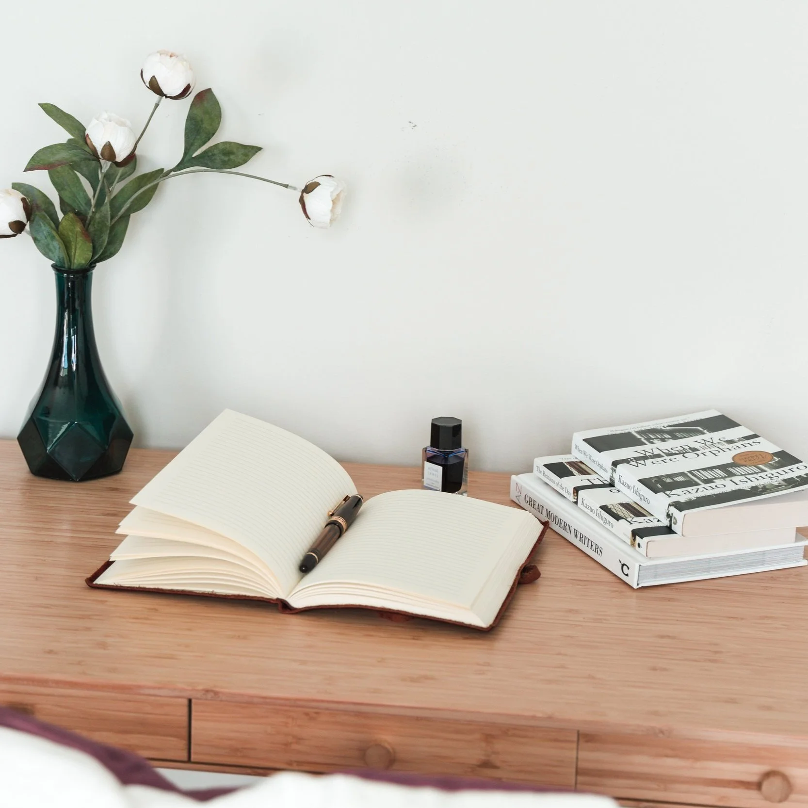 plusieurs livres dont un ouvert avec stylo et un vase sur un bureau