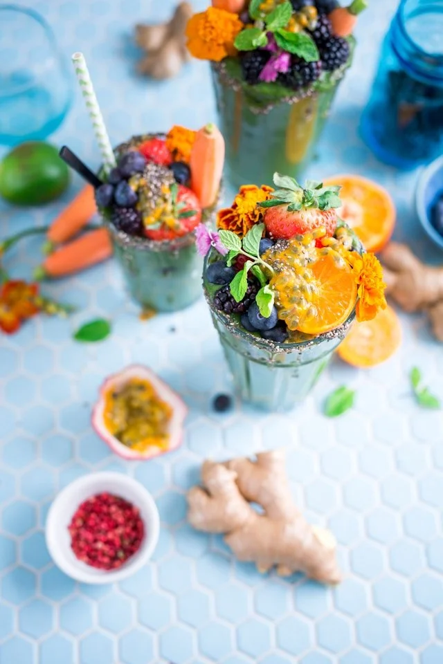 Trois verres de jus de fruits et légumes frais entourés de fleurs, fruits de la passion et de morceaux de gingembre pour stimuler l'appétit et soulager les nausées.