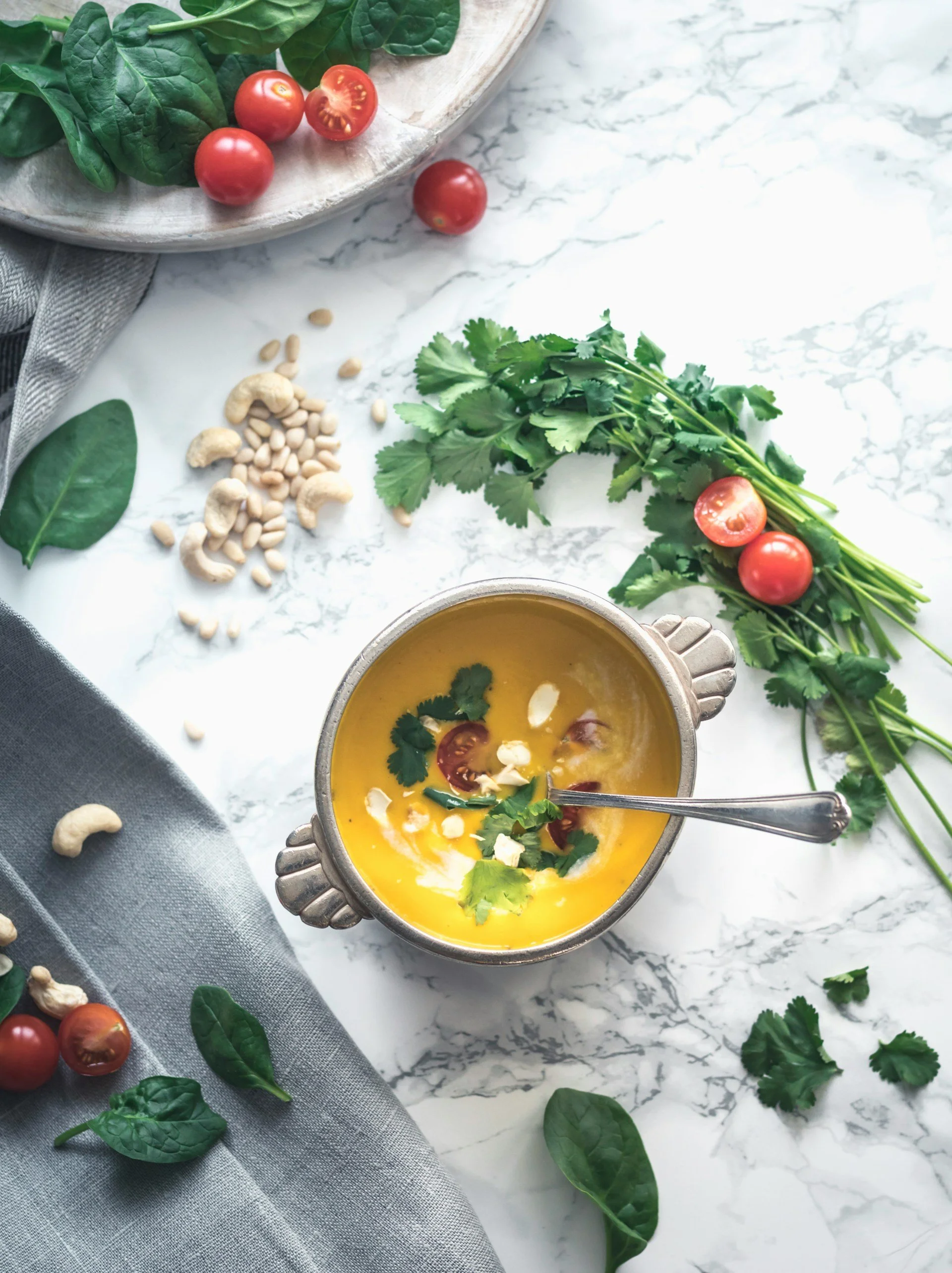 Un bol de soupe de courge orange parsemé de coriandre, de noix de cajou, de graines, de feuilles d'épinard et de châtaignes pour un repas texturé et calorique.