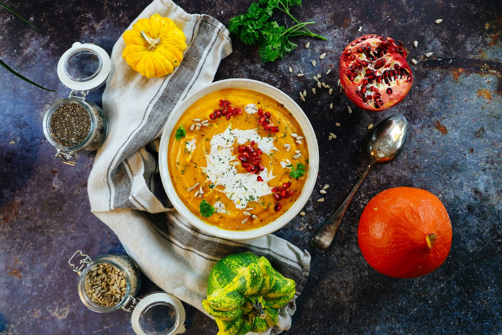 Soupe de courge vue de dessus avec graines de grenade, persil, crème et graines de chia et de tournesol, accompagnée de potirons, pour illustrer une alimentation réconfortante pendant la chimiothérapie