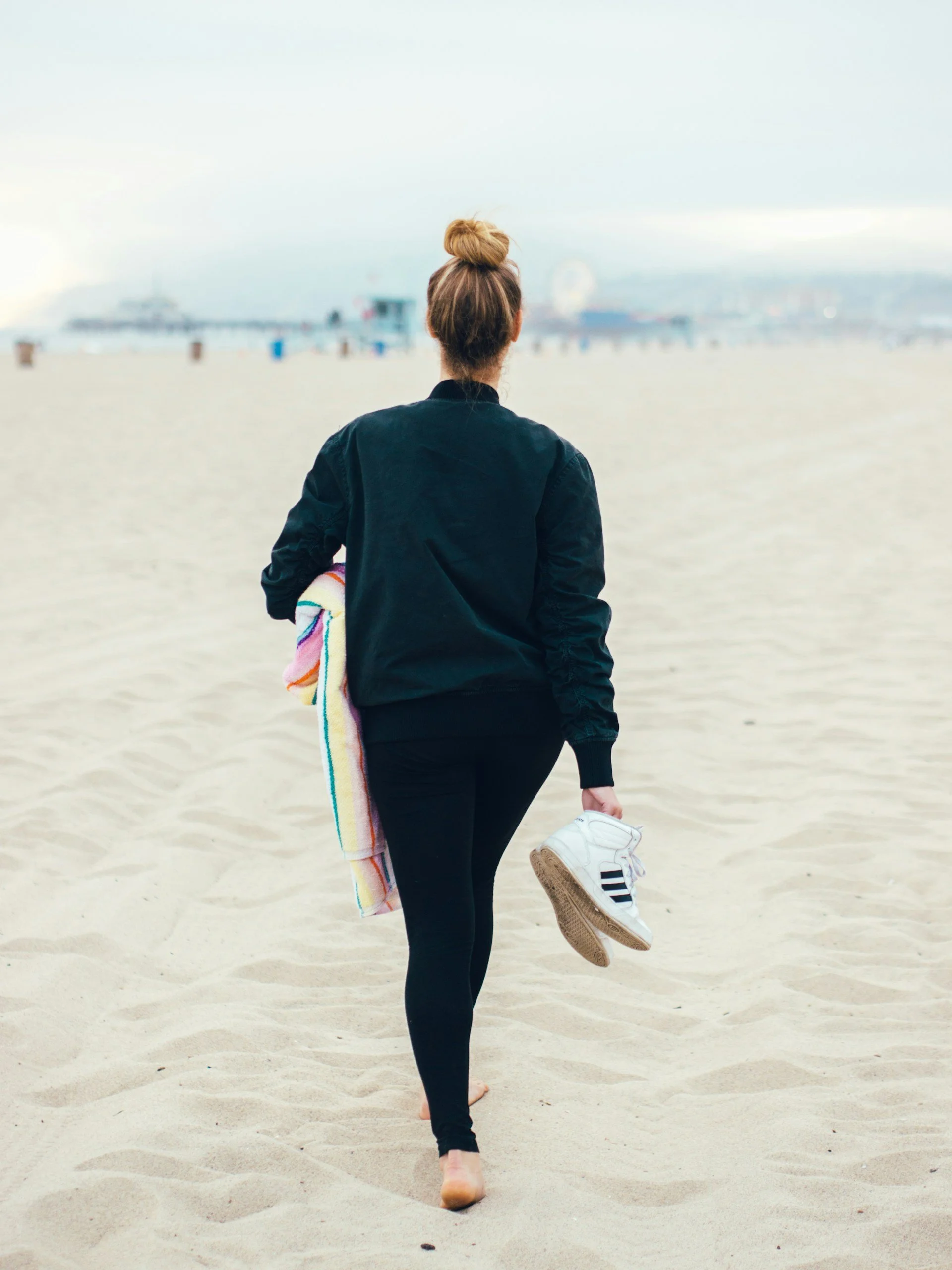 Femme marchand pieds nus sur le sable avec ses chaussures de sport à la main, illustrant la reprise progressive de l'activité physique après un cancer