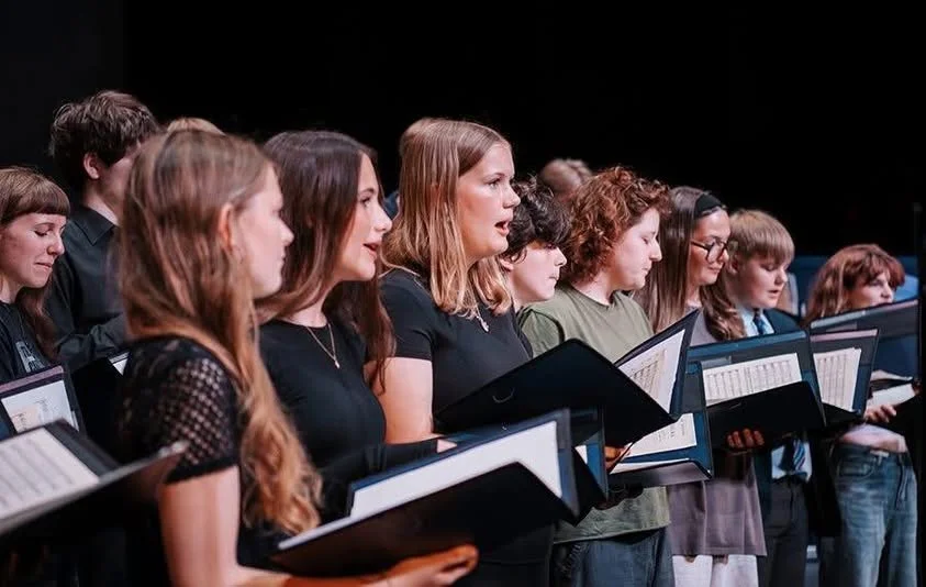 group of young people singing during the concert holding black folders with sheet music inside them