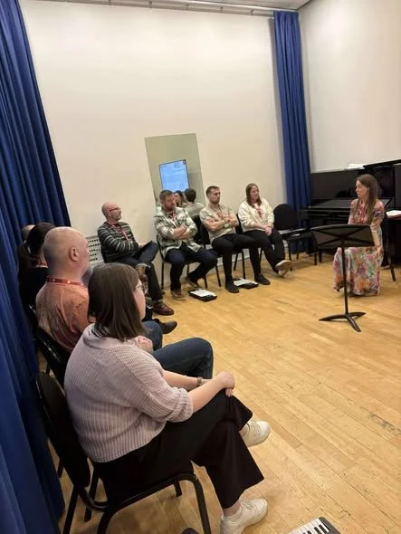 Facilitator sat at front of room with delegates sat in semi circle facing them.