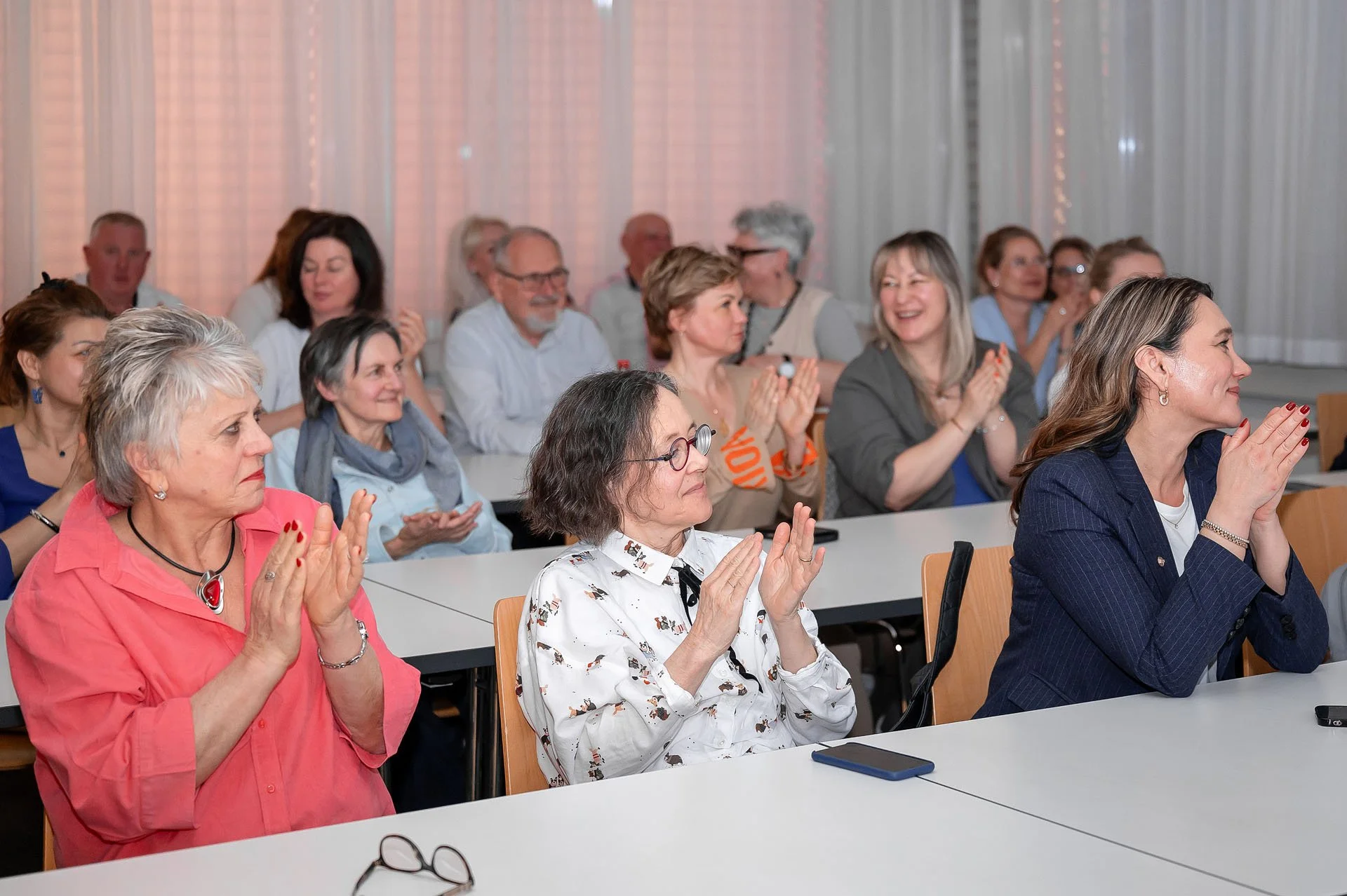 Menschen beim Applaus bei einer Veranstaltung in einem Saal mit weißen Vorhängen