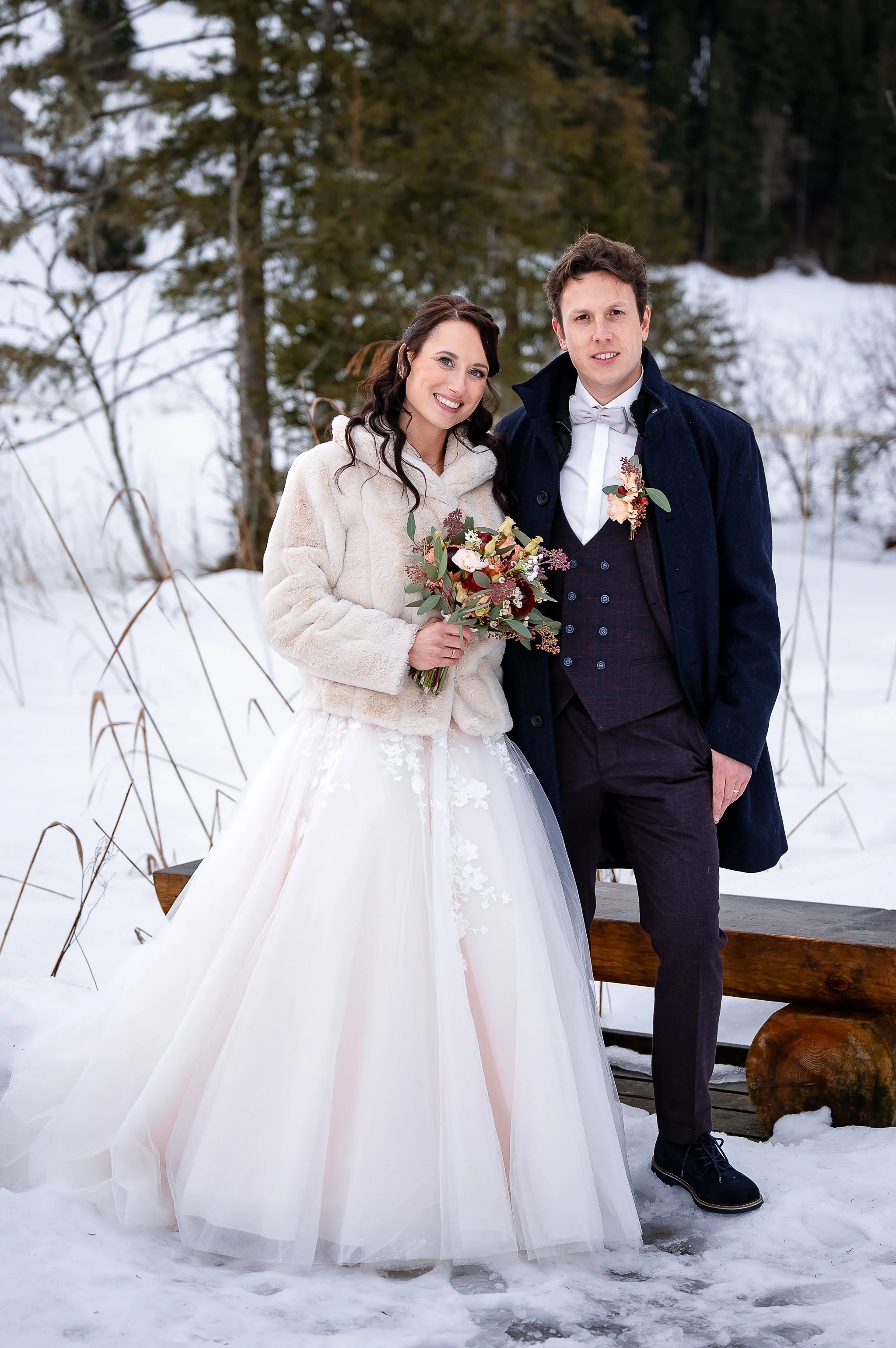 Ein Brautpaar im Schnee mit Schneelandschaft im Hintergrund.