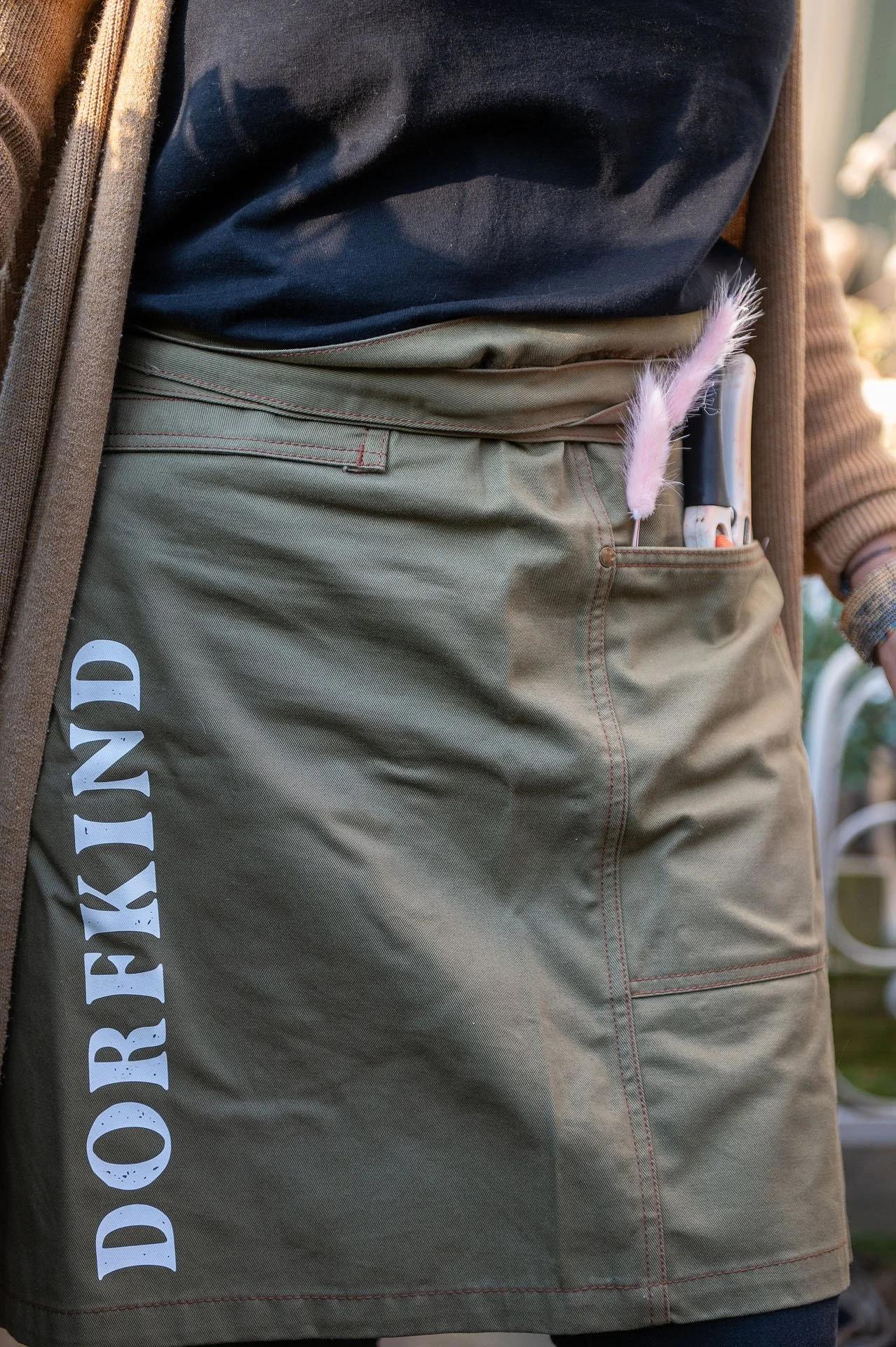 Nahaufnahme einer Person mit beige Hose, die einen kleinen rosa Plüschfeder und einen weißer Stift in der Tasche hat.