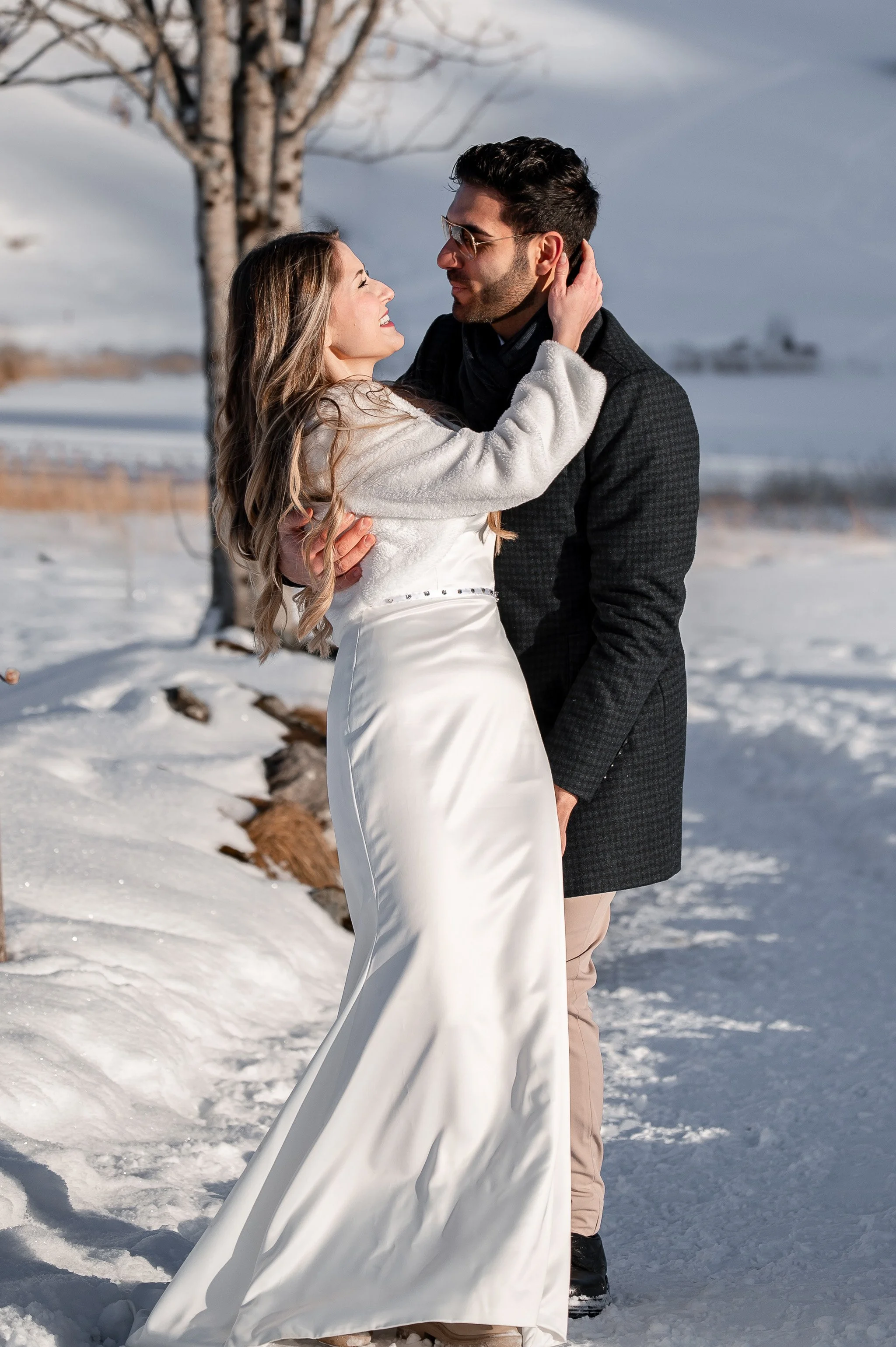Ein Brautpaar in Hochzeitskleidung, das sich im Schnee umarmt, bei schönem Winterwetter an einem winterlichen Tag.