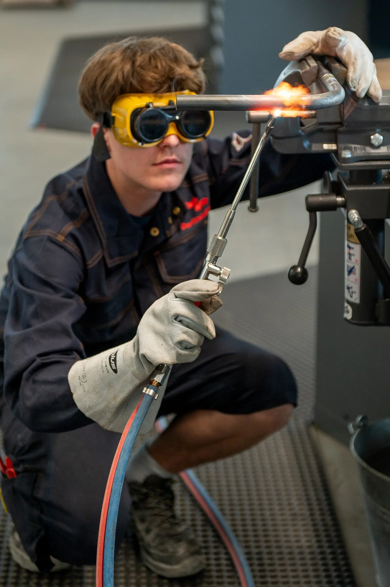 Ein junger Mann trägt Schutzbrille und Arbeitshandschuhe, während er einen Schweißbrenner zum Schweißen eines Metallrohrs verwendet.