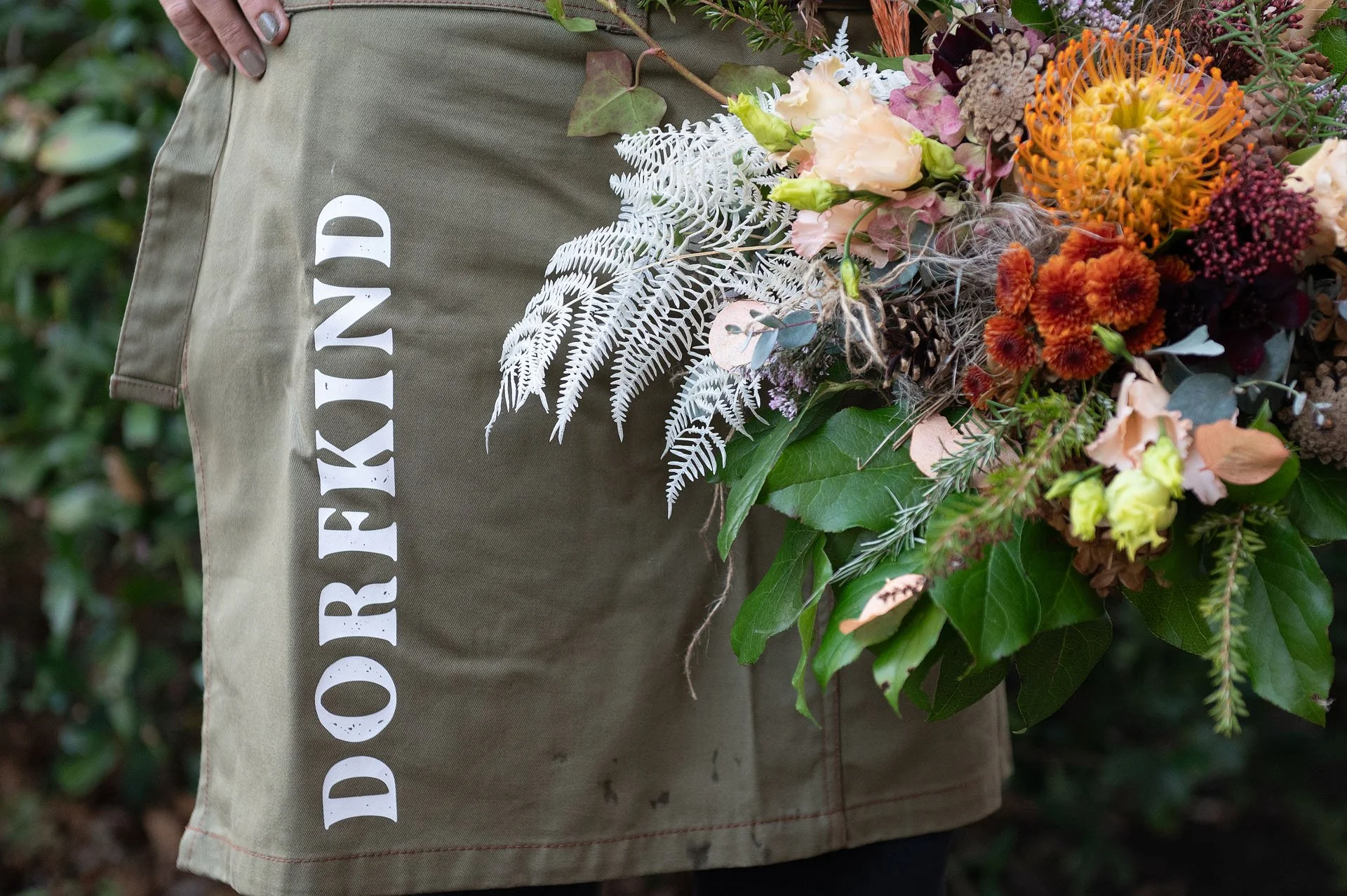 Person trägt eine grüne Jacke mit weißen Buchstaben. Auf der Jacke befindet sich ein Blumenstrauß mit bunten Blumen und grünen Blättern.
