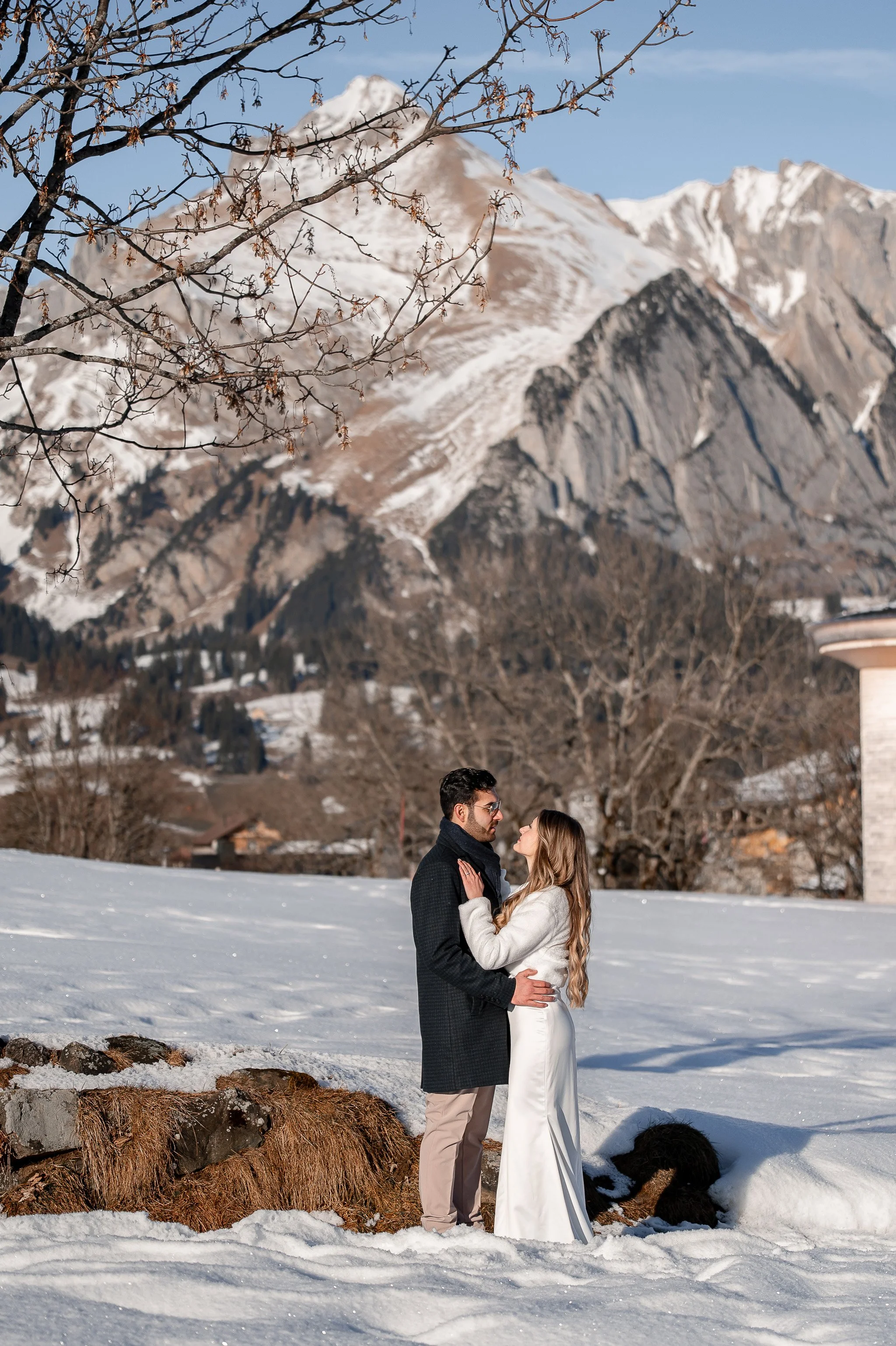 Ein Brautpaar steht sich auf schneebedecktem Gelände gegenüber, umgeben von Winterlandschaft mit Bergen im Hintergrund.