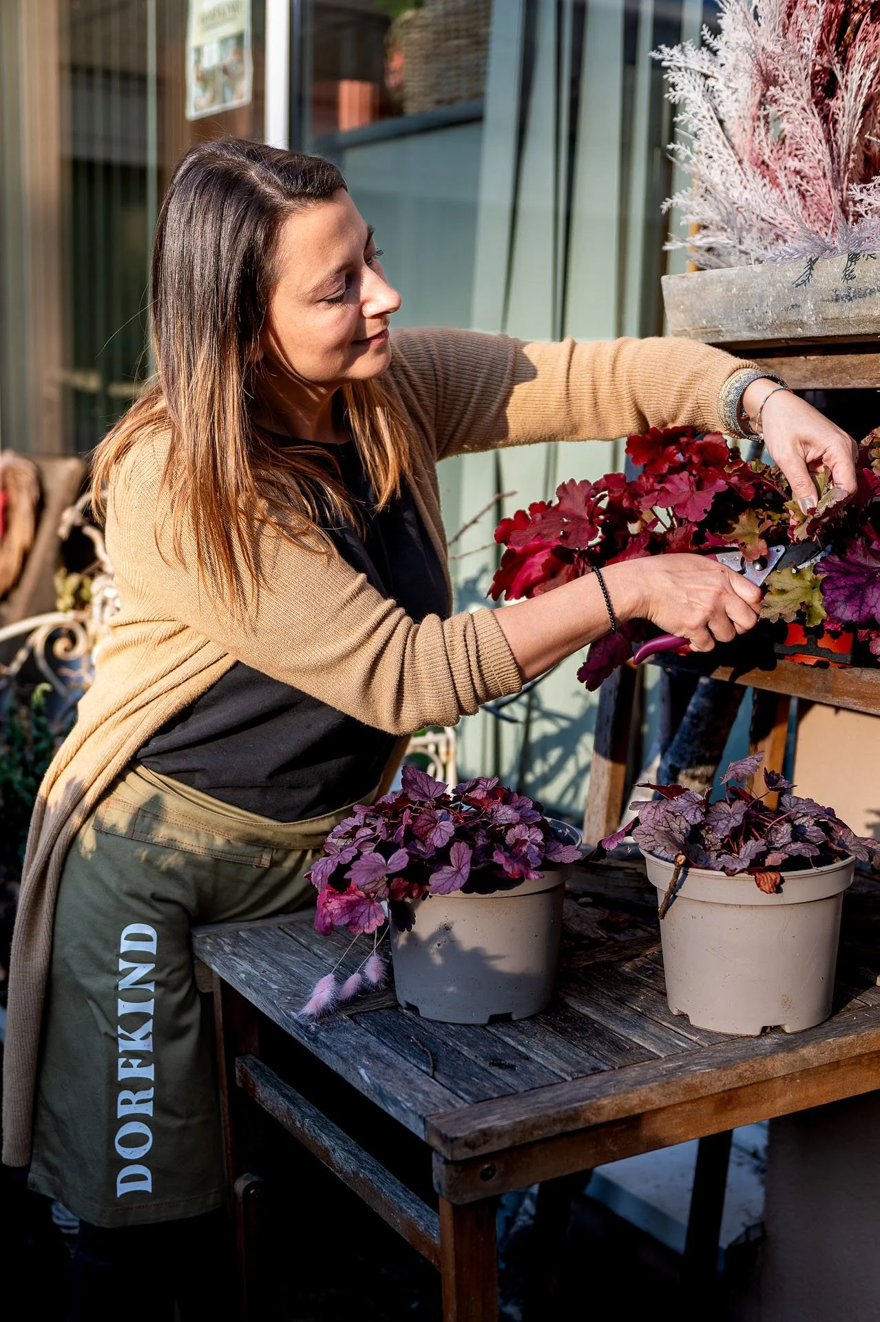 Frau beim Umgang mit roten und lila Blumen in Töpfen auf einem Holztisch im Freien.