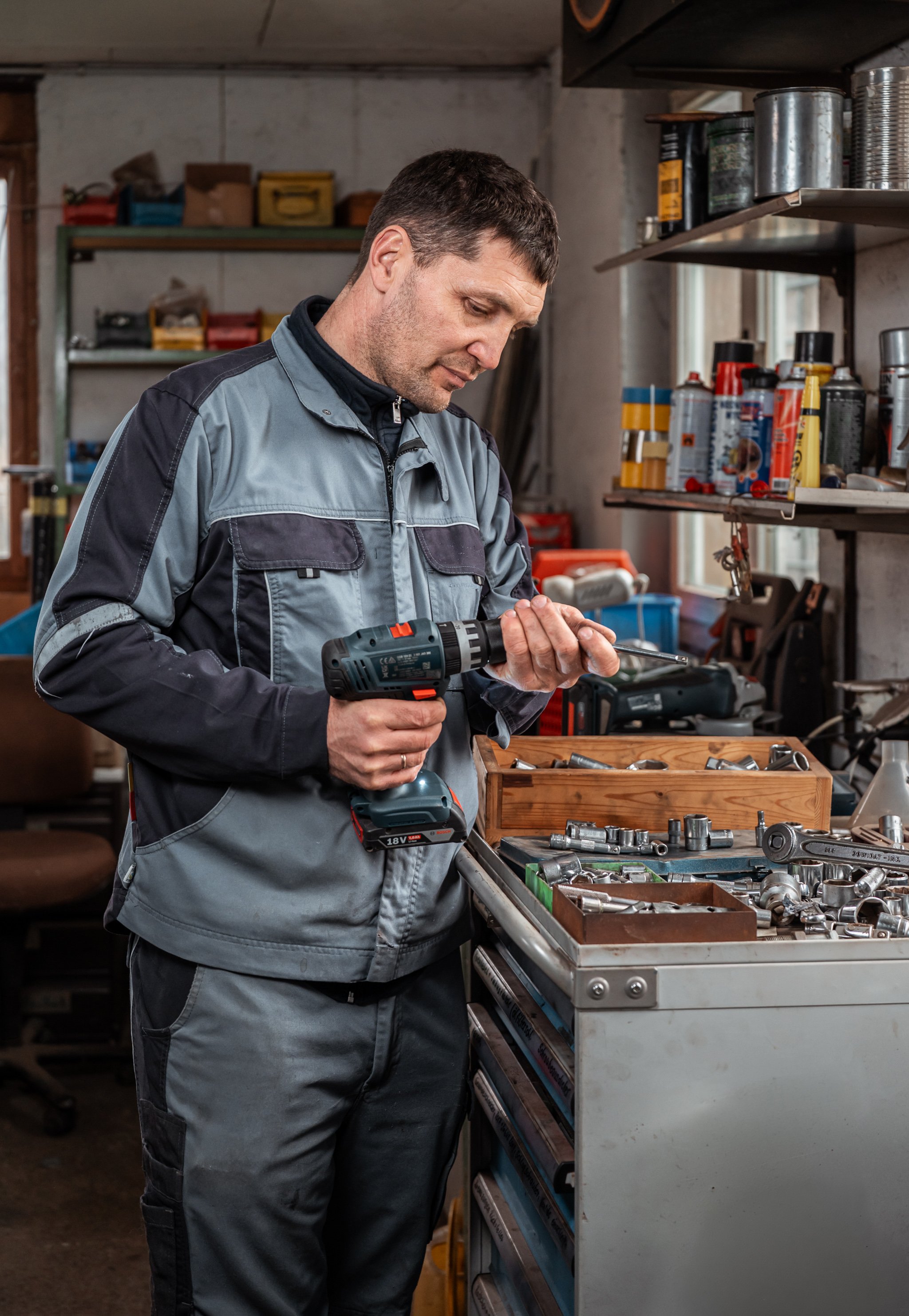 Mann in Arbeitskleidung arbeitet mit einem Akku-Bohrer in einer Werkstatt an einer Werkzeugschale mit Metallteilen.