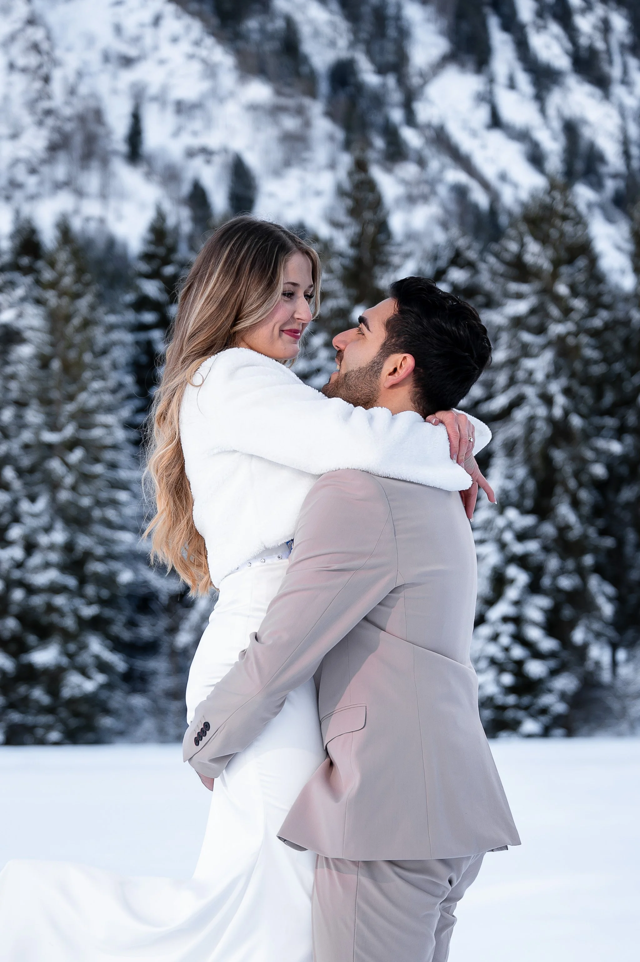 Ein Brautpaar umarmt sich in einer verschneiten Winterlandschaft.
