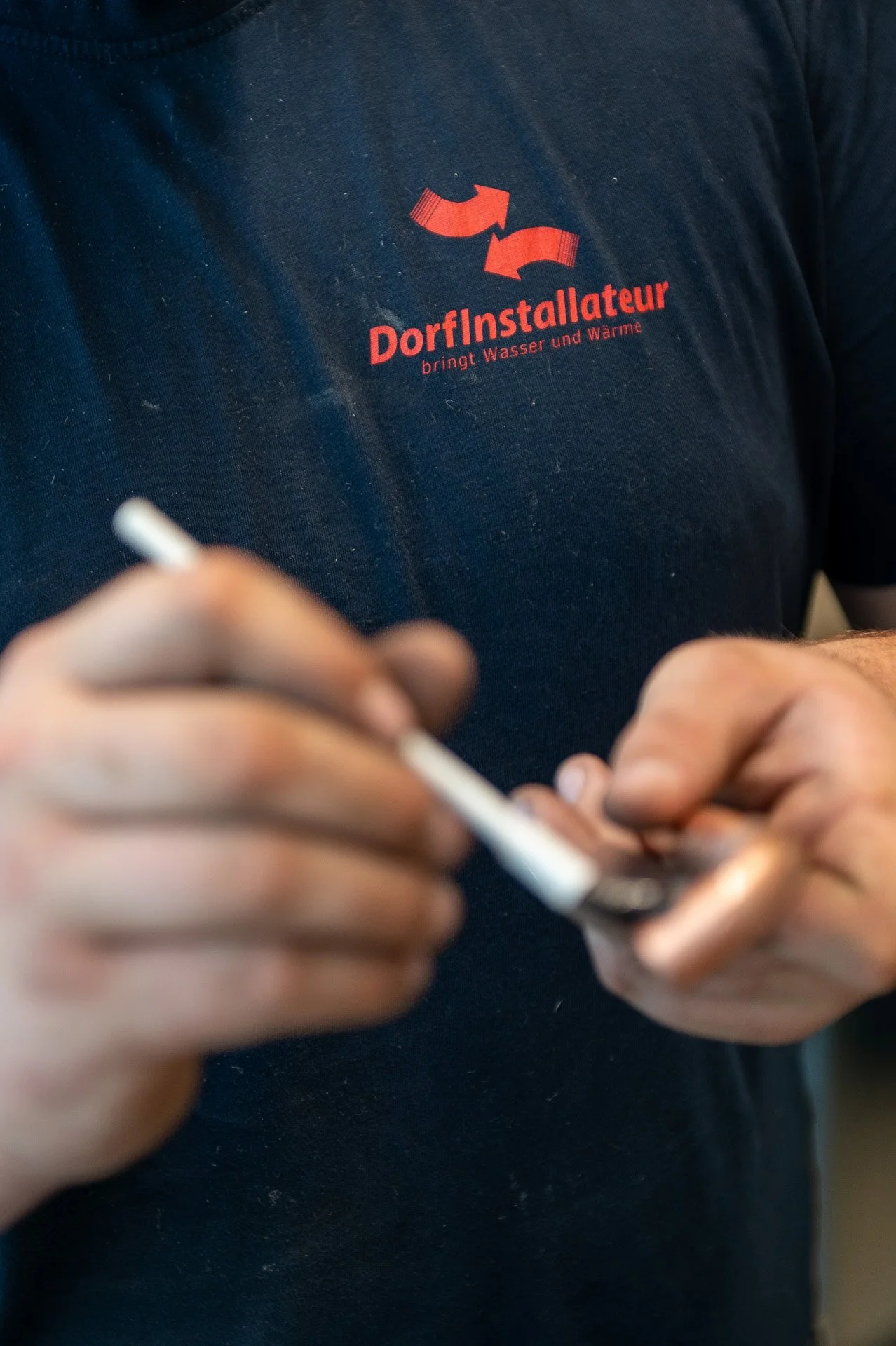Nahaufnahme eines Mannes in einem schwarzen T-Shirt mit rotem Logo, der an seinem Smartphone arbeitet, das in beiden Händen hält.