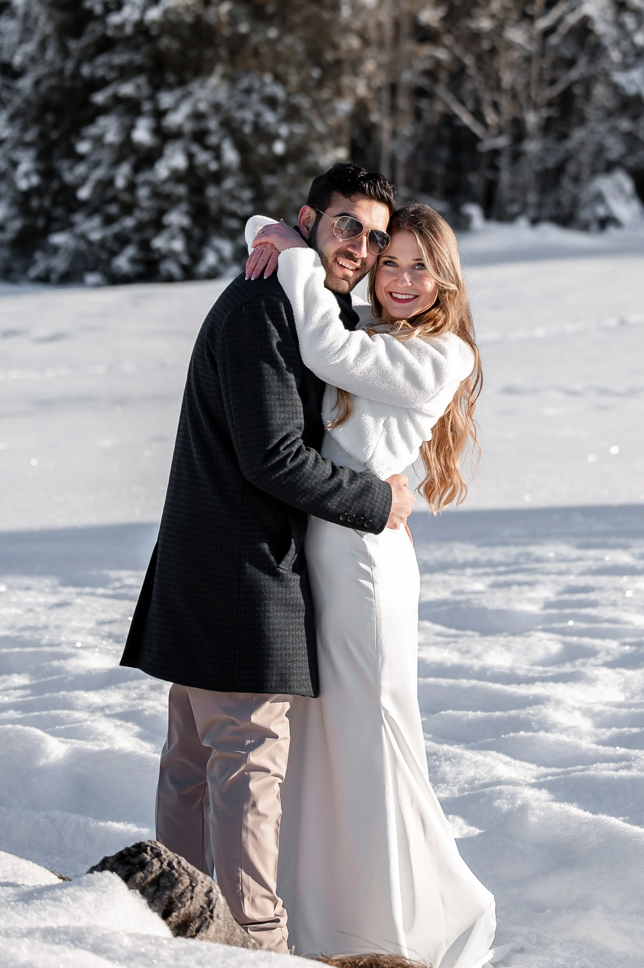 Ein Brautpaar in Hochzeitskleidung umarmt sich lachend im Schnee.