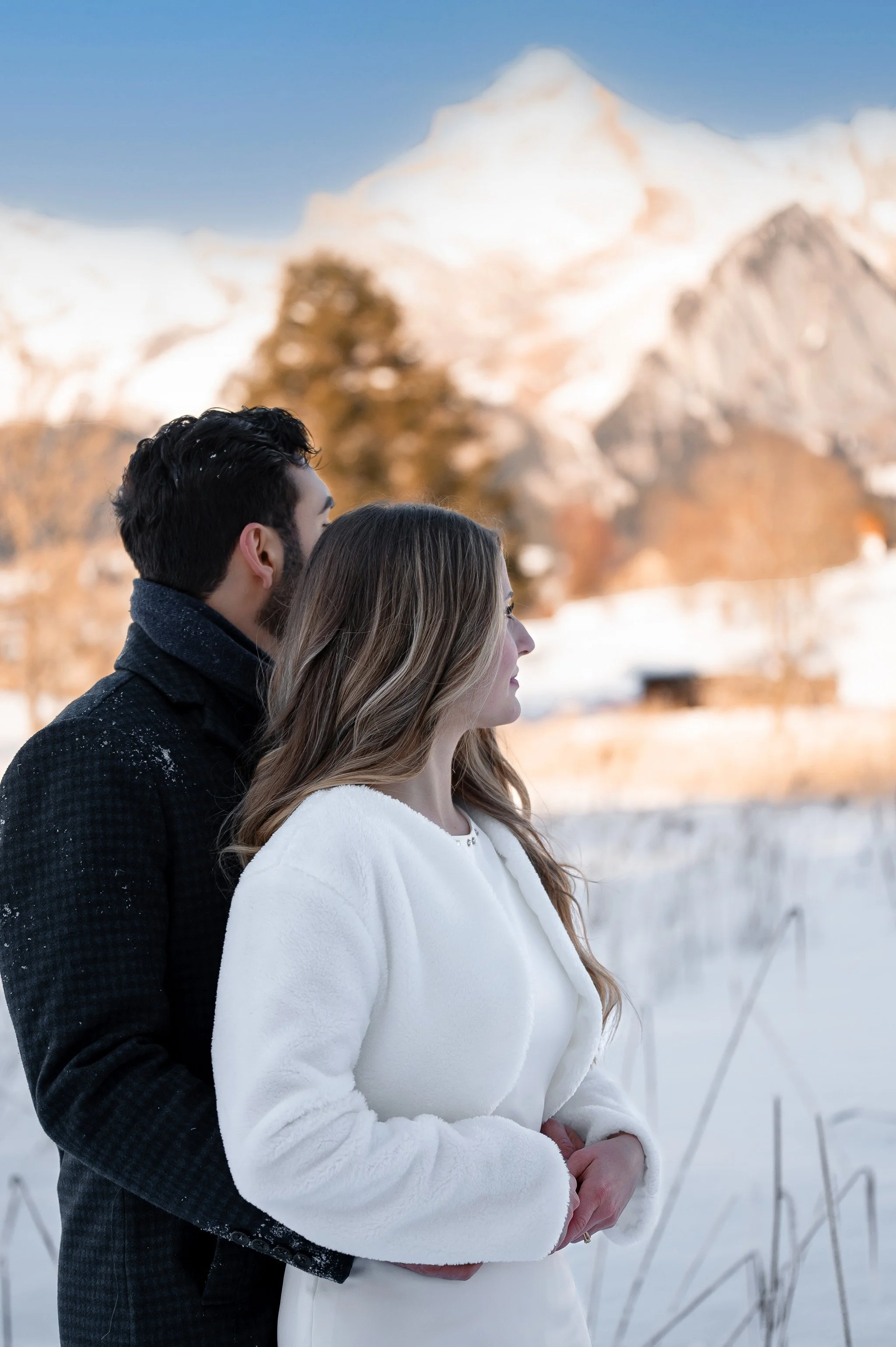 Ein Brautpaar steht in einer verschneiten Winterlandschaft mit Bergen im Hintergrund.