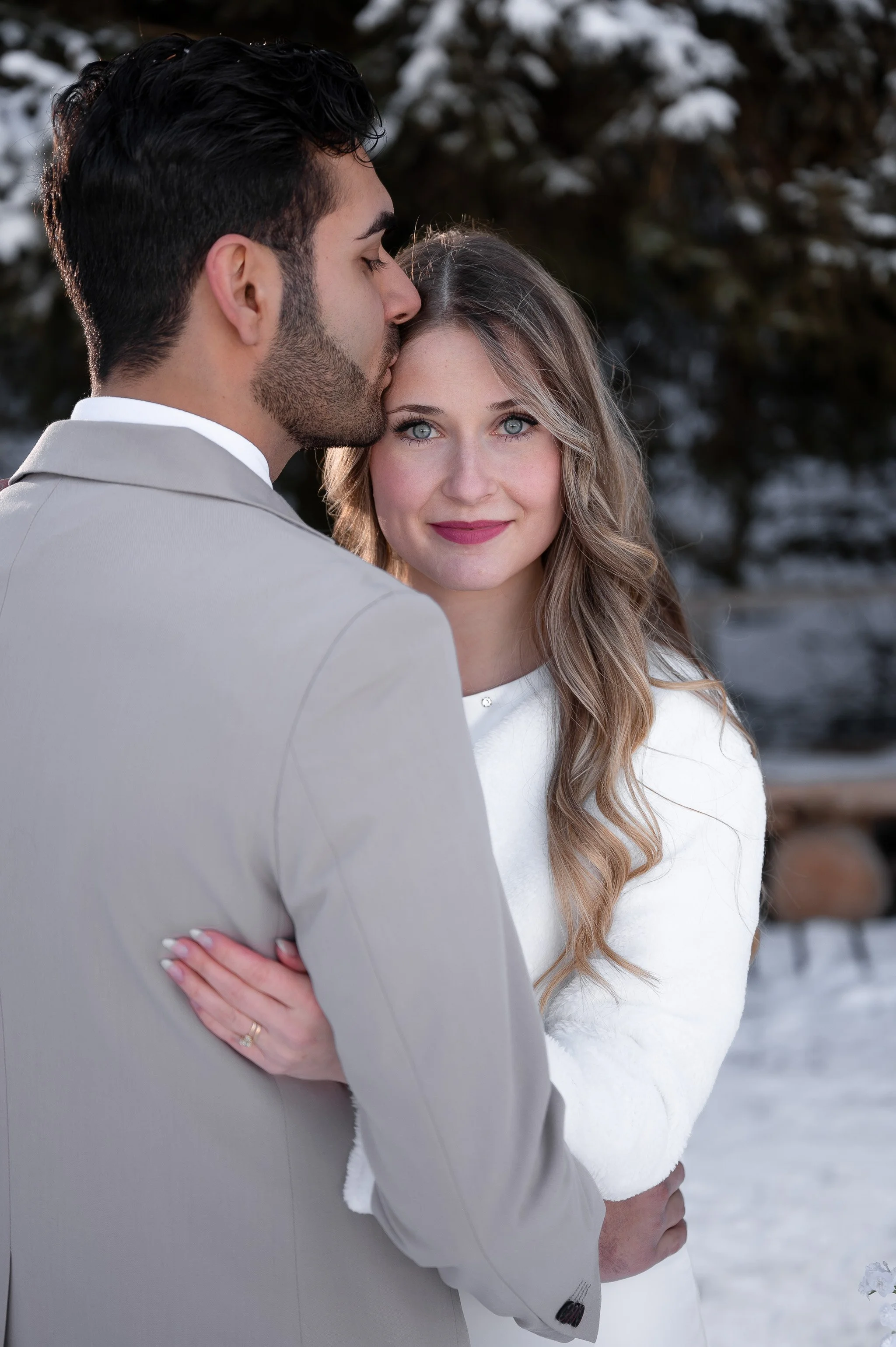 Ein Brautpaar steht im Schnee, der Mann küsst die Frau auf die Stirn.