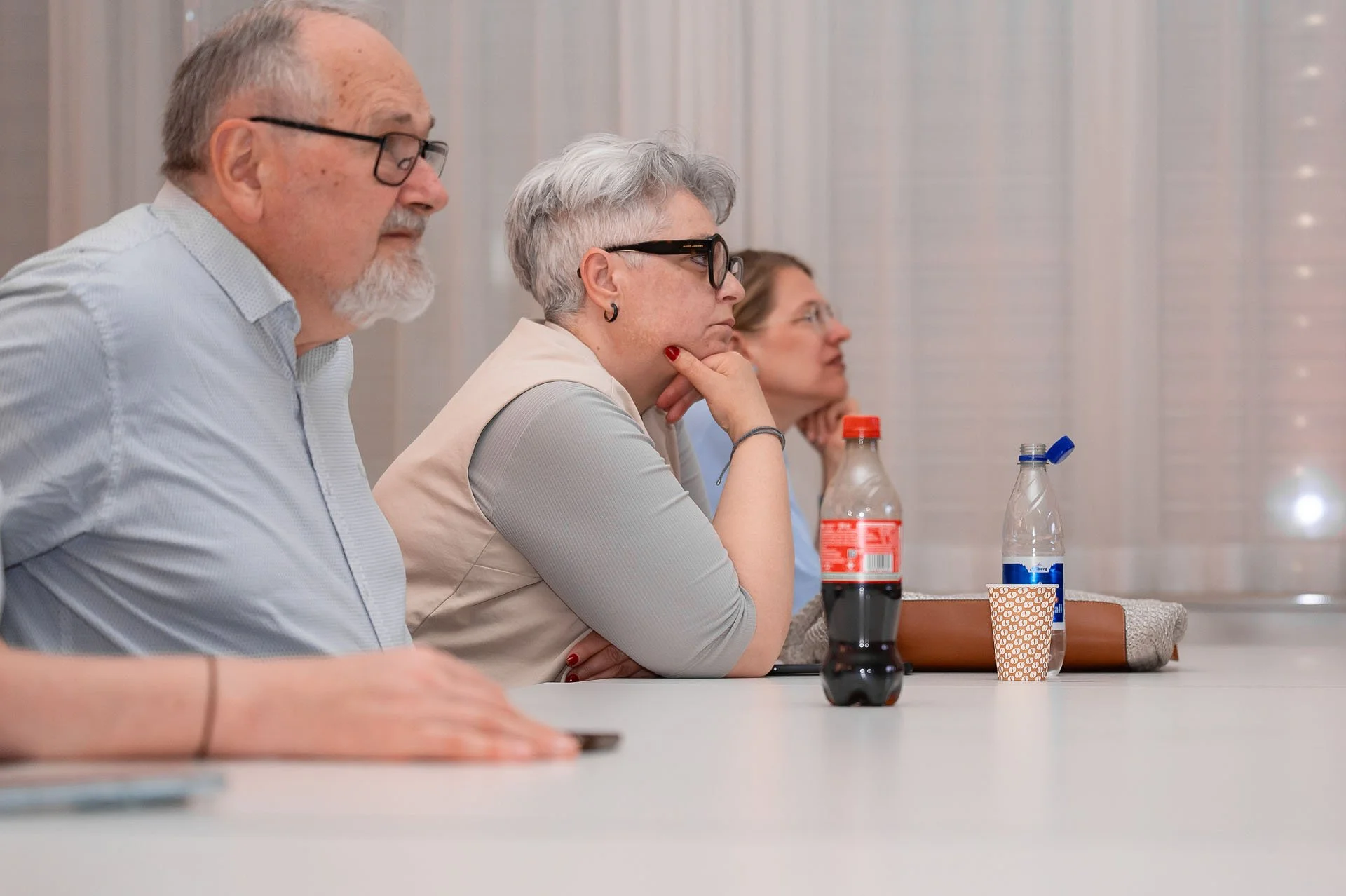 Menschen sitzen an einem Tisch bei einer Besprechung, trinken Cola und haben Pappbecher vor sich.