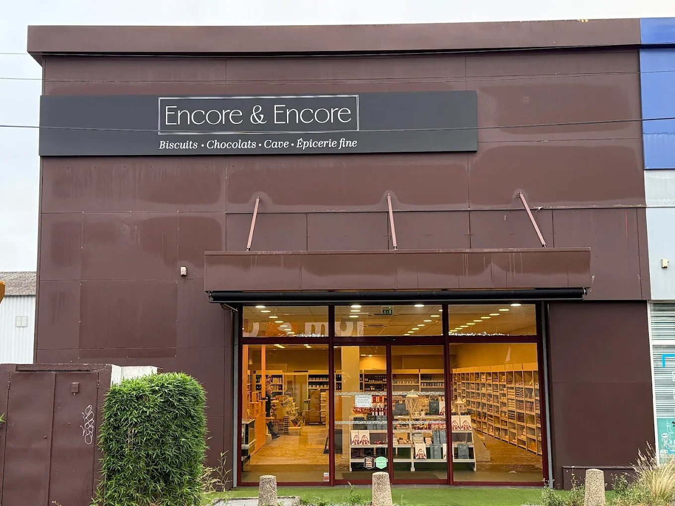 Façade d'un magasin Encore & Encore à Saint Grégoire , spécialisé en biscuits bretons , chocolats français, cave et épicerie fine, avec une grande vitrine montrant l'intérieur bien éclairé et des étagères remplies de produits.