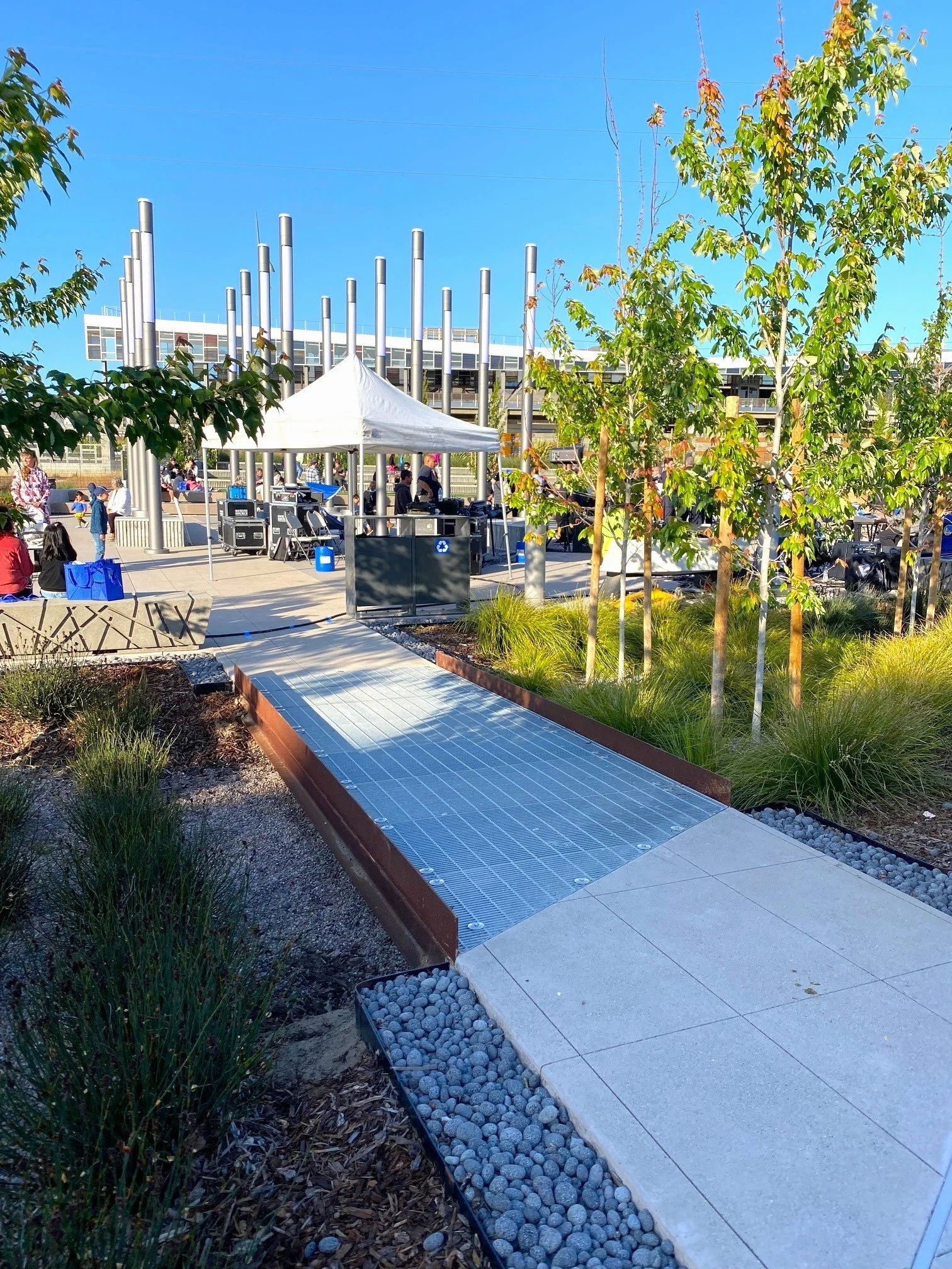 A wide pathway extends over a stormwater area and facilitates circulation through the plaza, which can be used to host community events. 