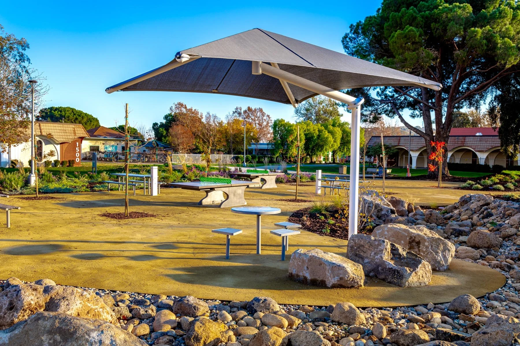 Shade structures and open seating areas create comfortable outdoor rooms that support social interaction while framing views across the reimagined quad.
