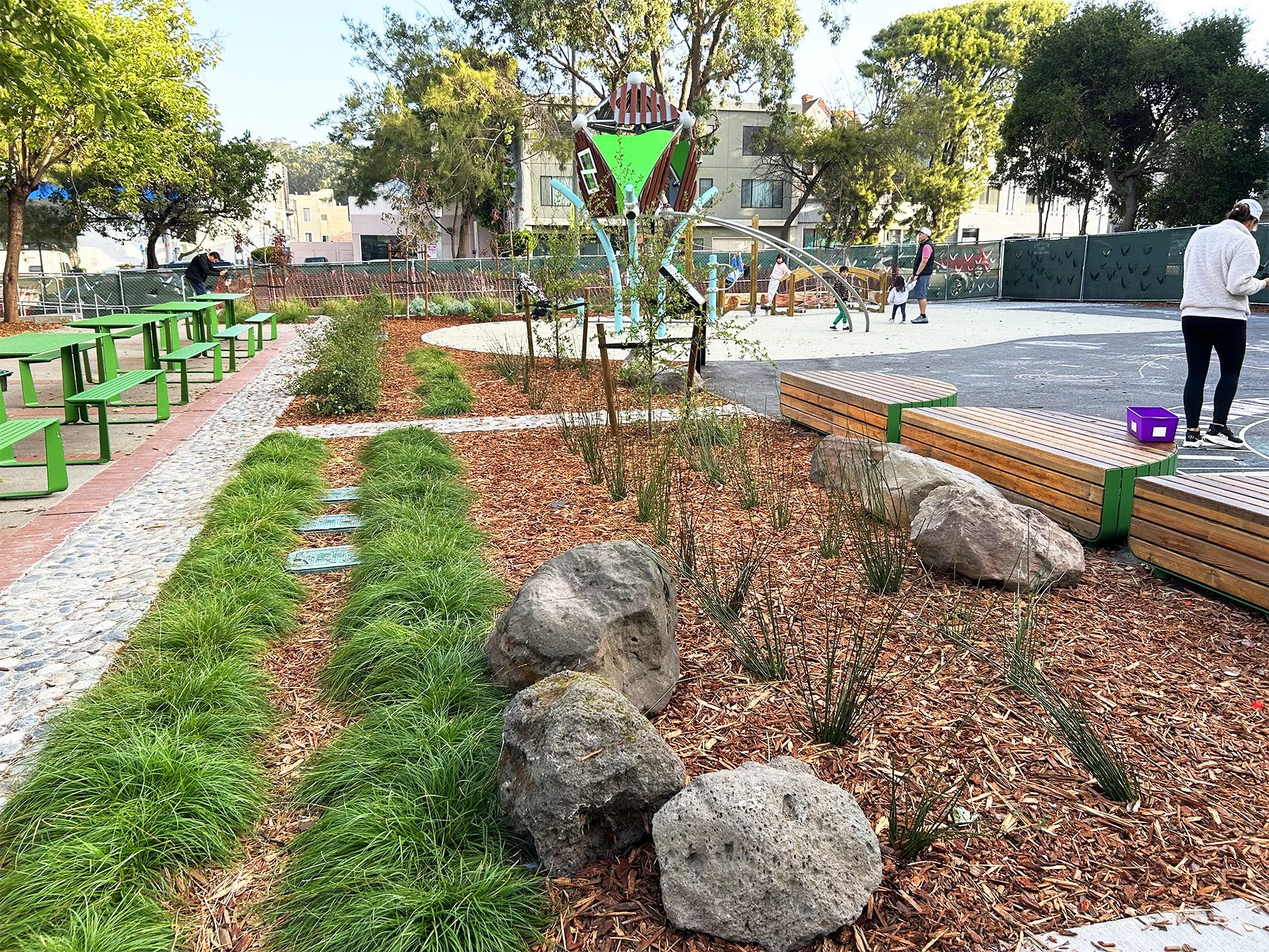 In the kindergarten yard, flexible play spaces, vibrantly colored benches, wood seating, and layered planting create inviting outdoor spaces designed for exploration.