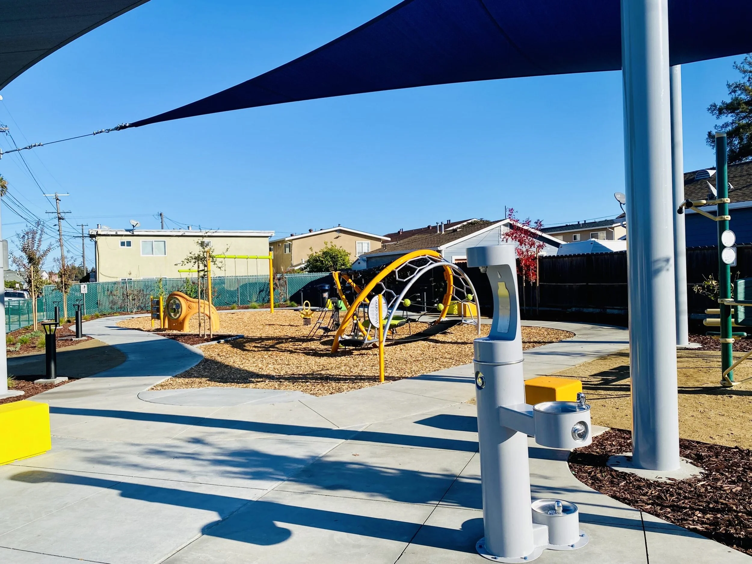 Shade canopies and colorful, integrated recreation elements create a flexible neighborhood space designed for play, movement, and everyday community use.