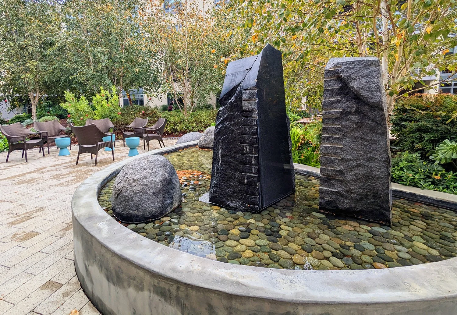 Water glides across stone and rock in the courtyard's central fountain. Framed by shrubs and trees, this focal element offers serene sights and sounds.