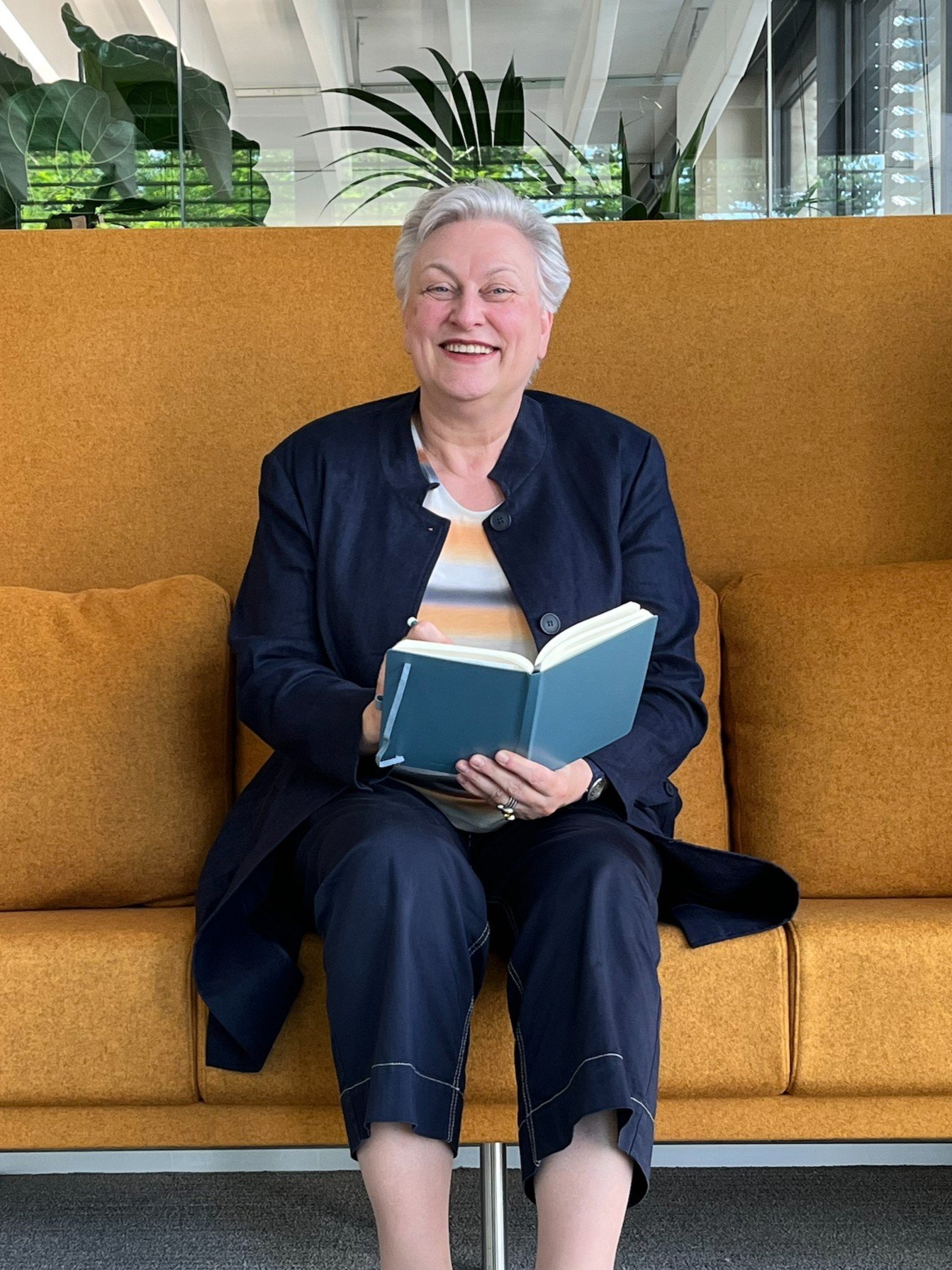 Uta sitzt auf einem gelben Sofa und hält ihr Notizbuch in den Händen