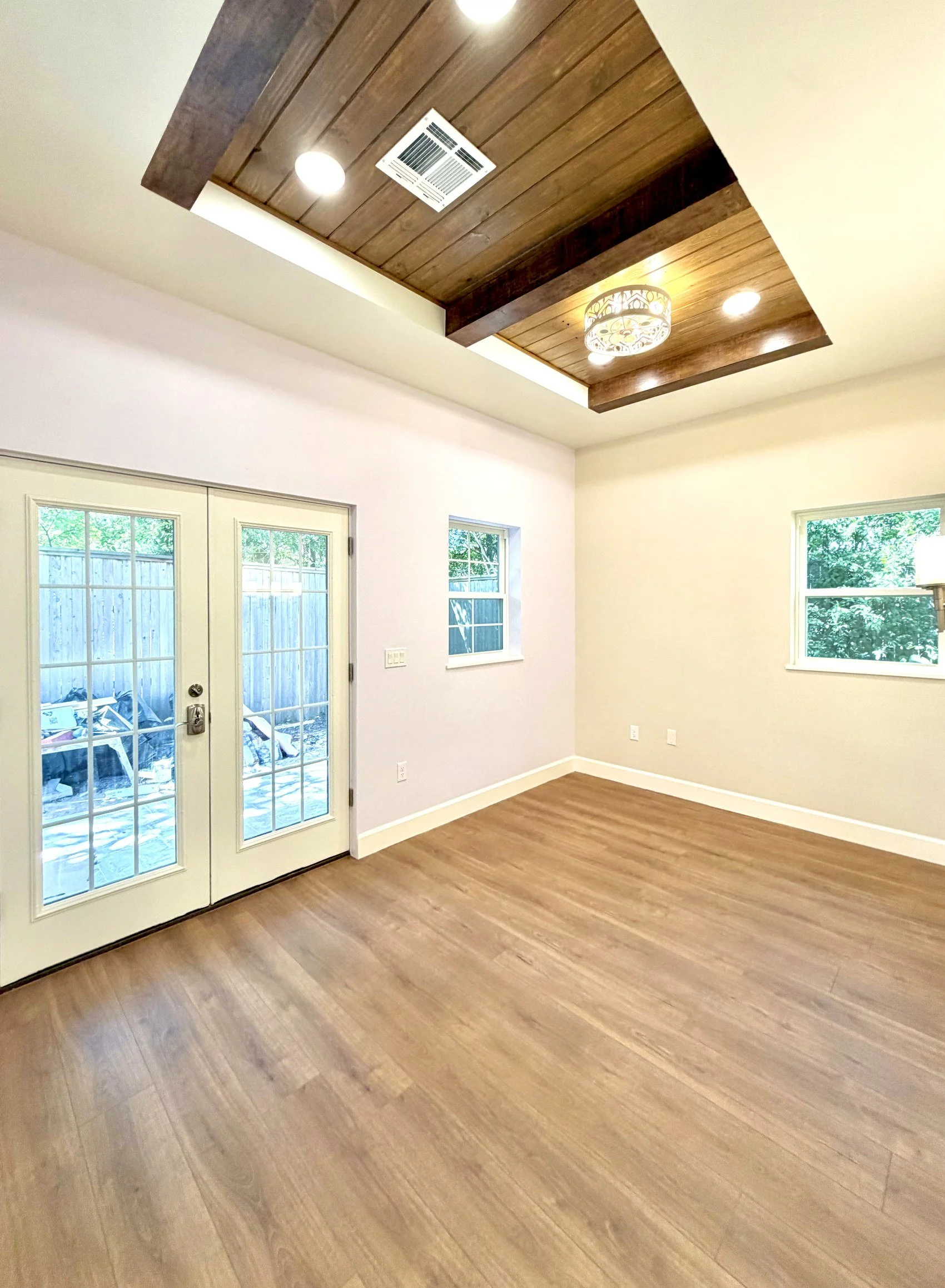 Empty room with hardwood floors, white walls, two large windows, and a double door leading outside