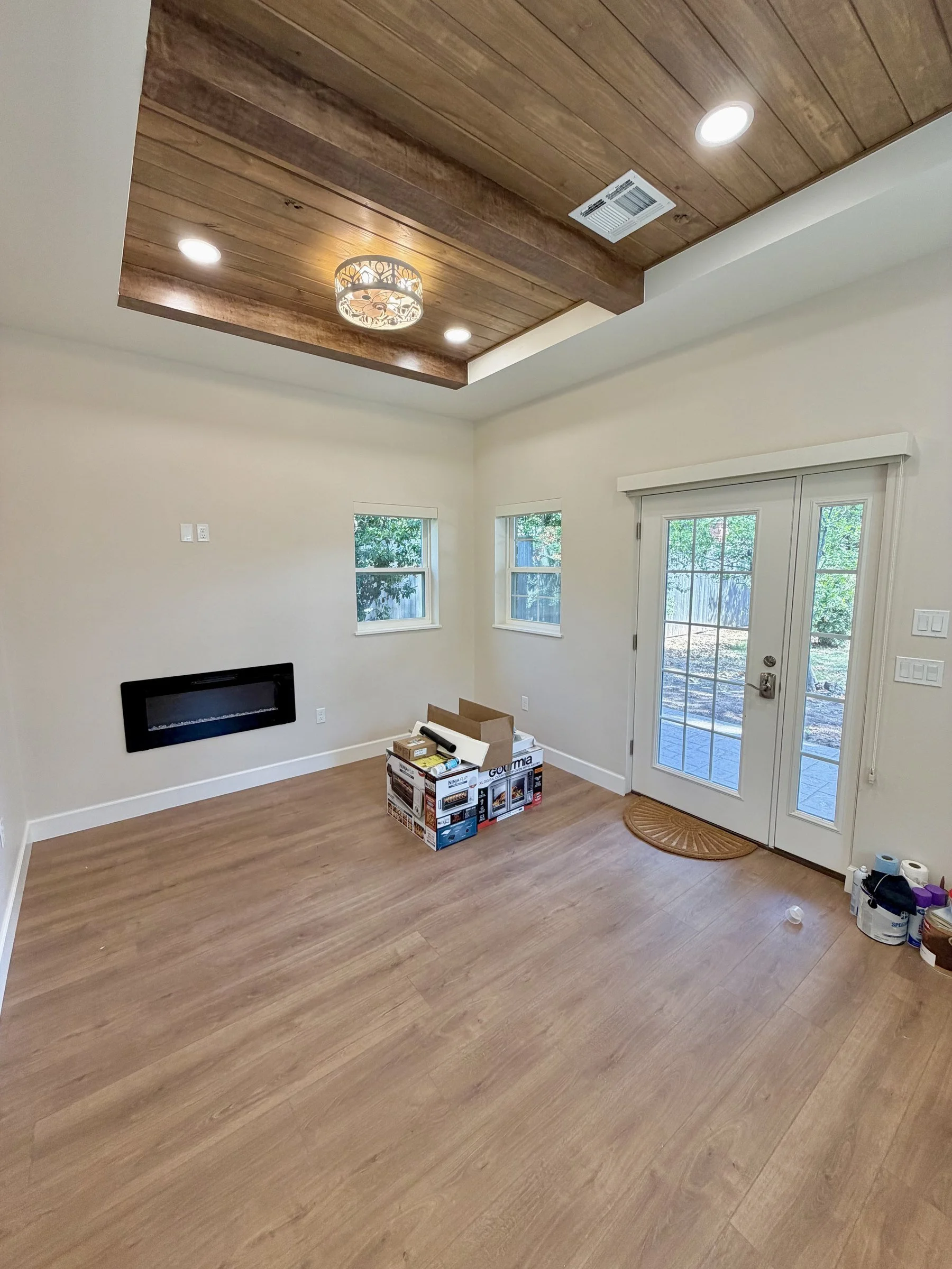 Living room with new wooden flooring, two small windows, a set of double glass doors, and a partial view of tools and materials for renovation or flooring installation.