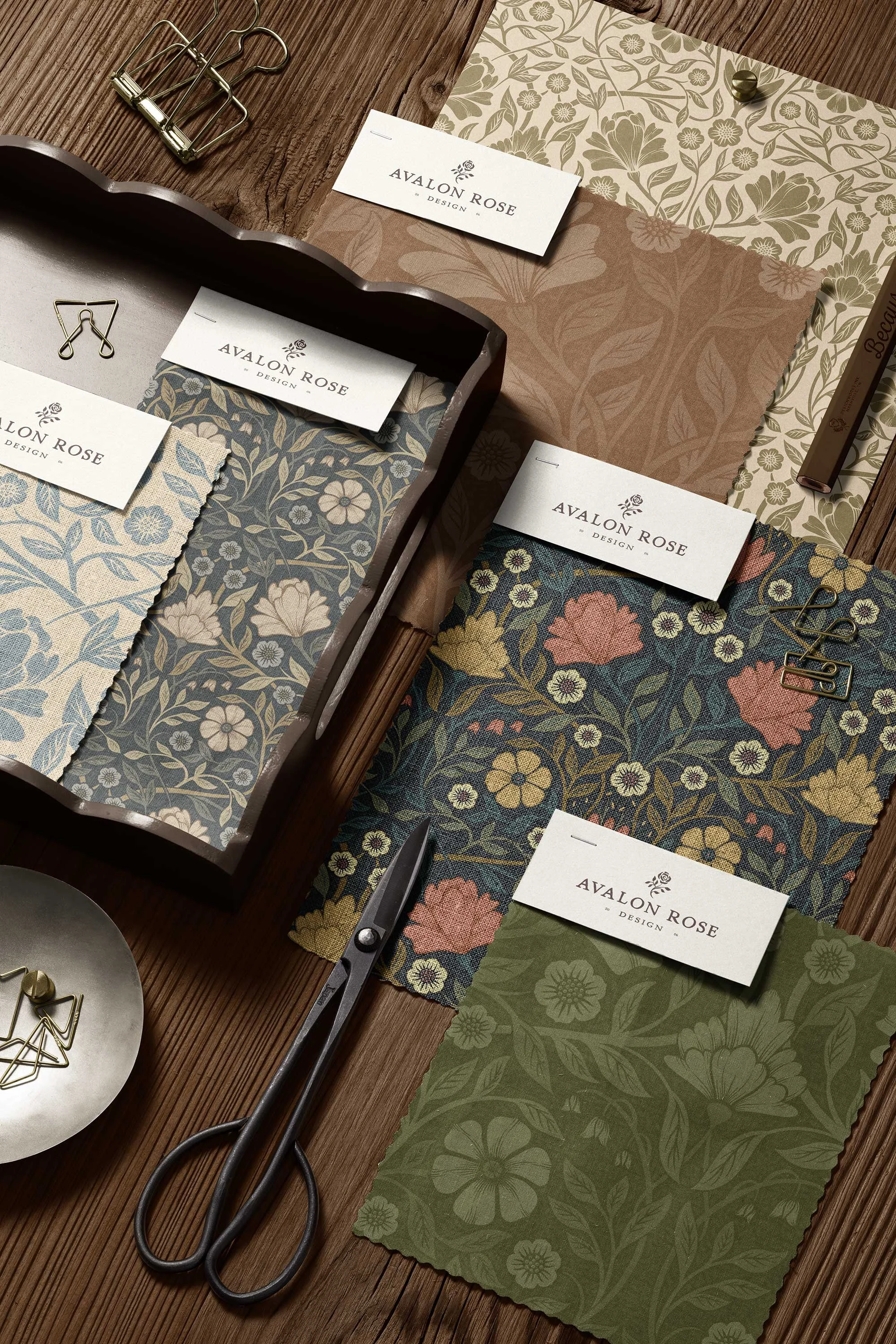 Fabric samples with floral patterns, scissors, paper clips, and branding cards for Avalon Rose Design displayed on a wooden surface.