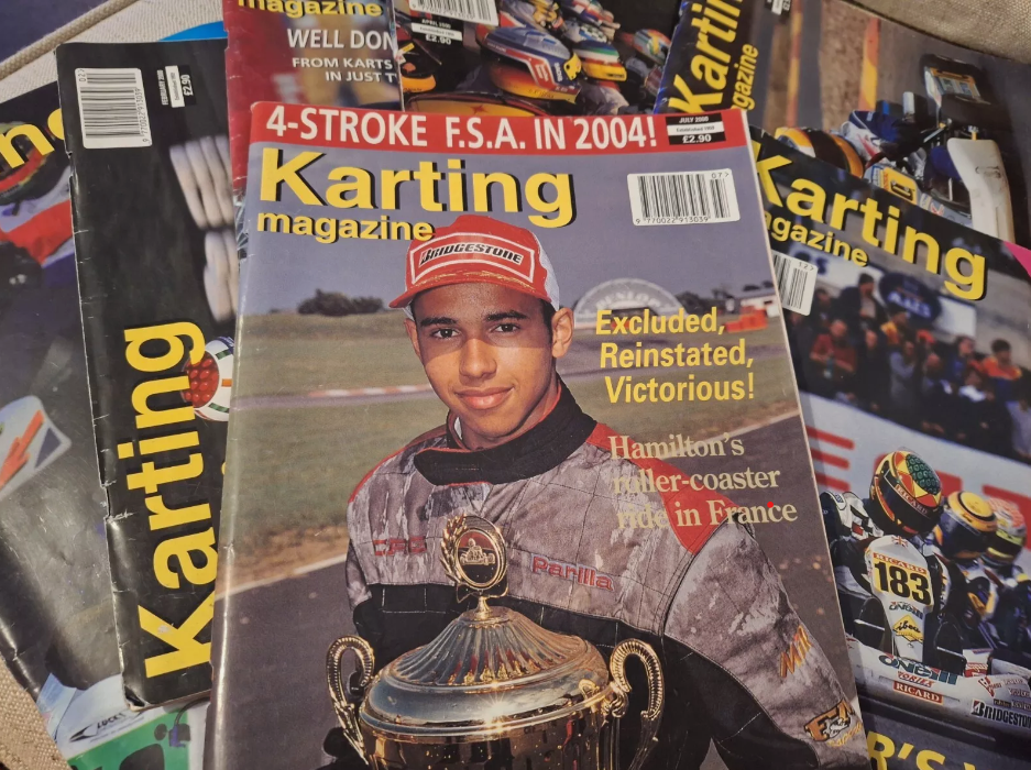 A stack of karting magazines featuring a young race car driver in a grey racing suit and red cap holding a trophy.