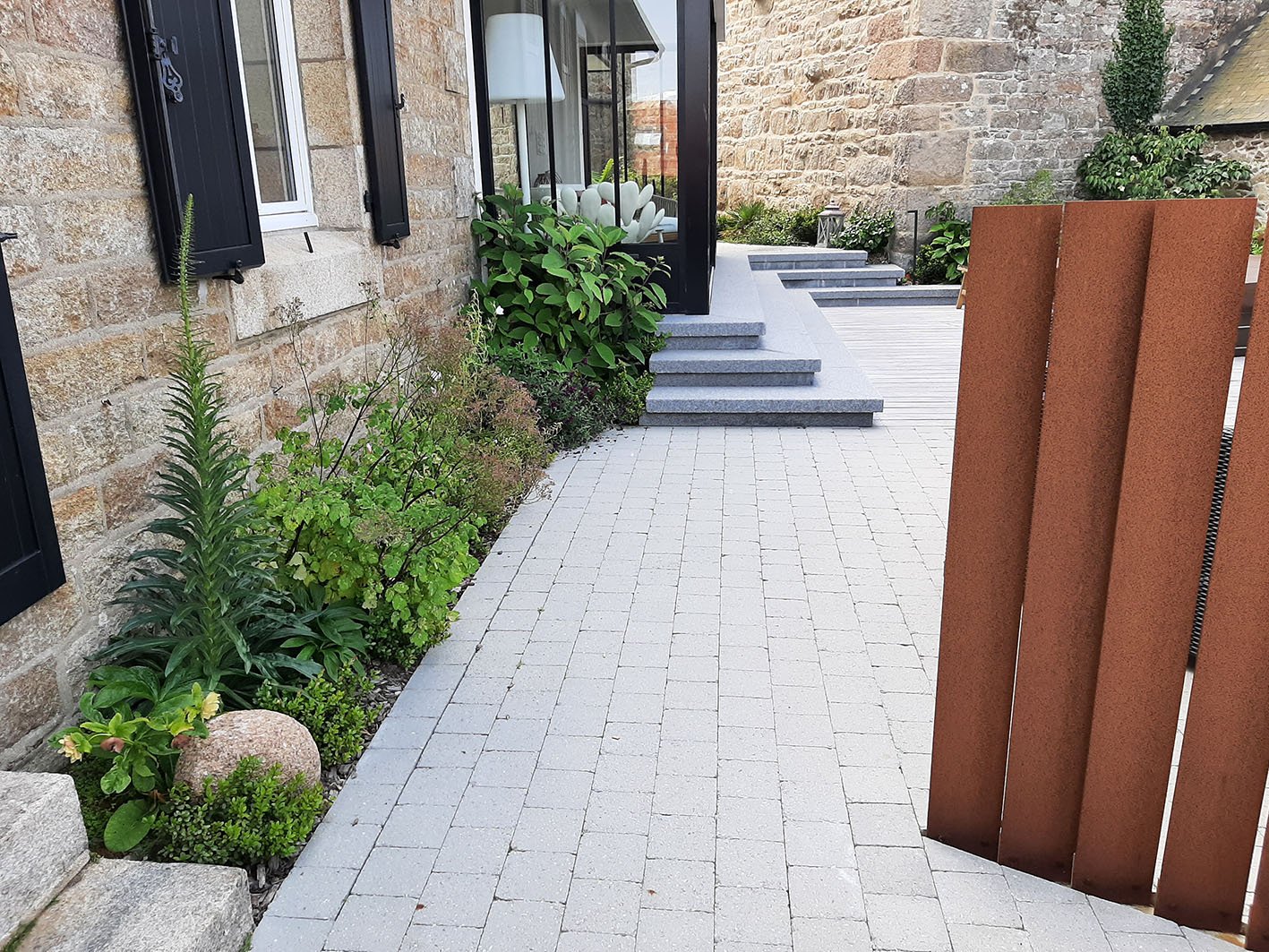 Aménagement d'un petit jardin de ville à Trébeurden : pavés, claustras en acier corten et vivaces devant une maison en pierre rénovée.