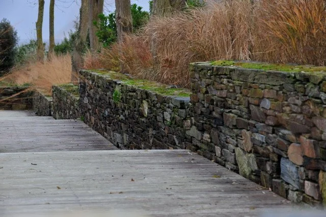 Jardin urbain et de bord de mer à Cancale avec travail de la pente en terrasses en bois et murs en pierre sèche.