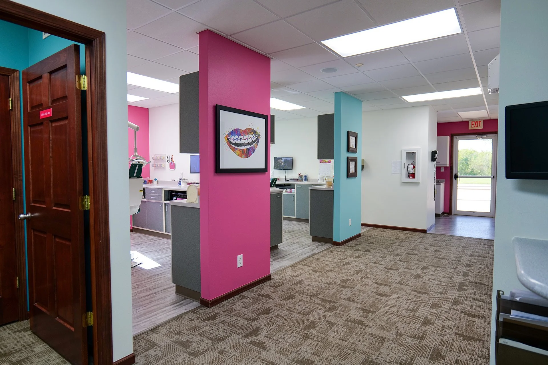 Colorful dental office with pink and blue walls, reception desk, and dental chairs visible in the background.