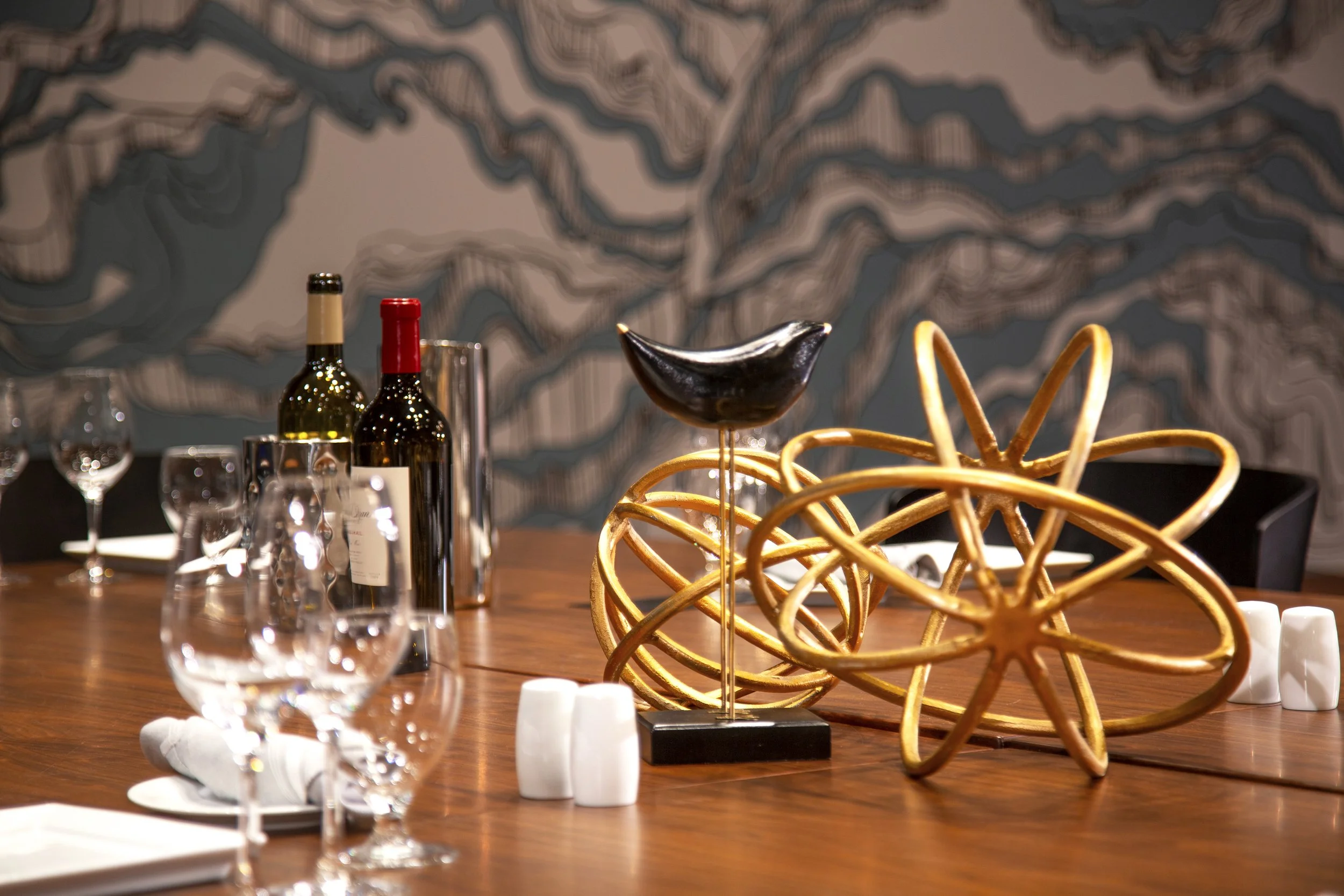 Elegant dining table with wine bottles, wine glasses, and decorative sculptures on a wooden surface.