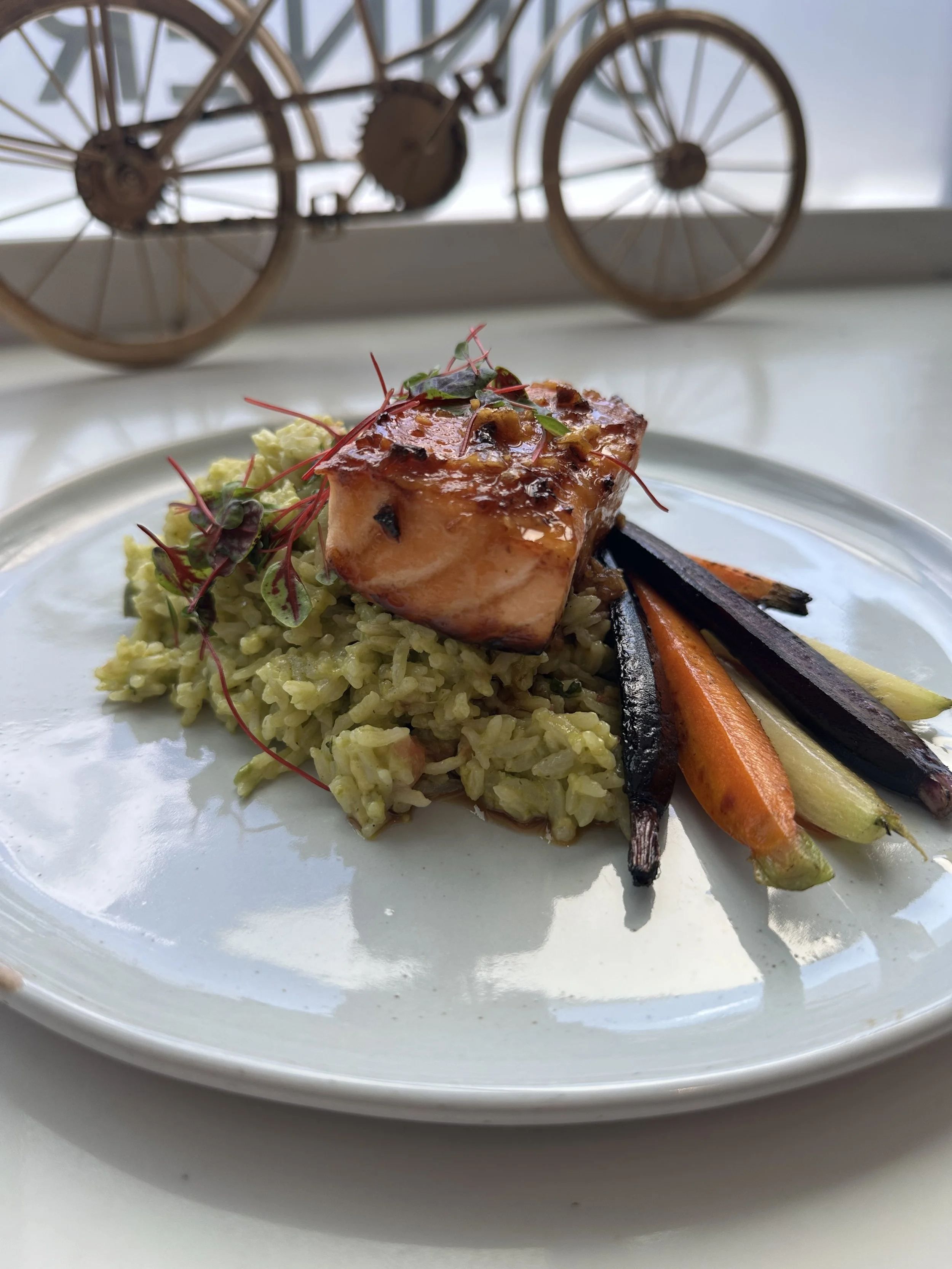 A plated serving of grilled salmon with roasted vegetables and rice, garnished with microgreens, on a white plate.
