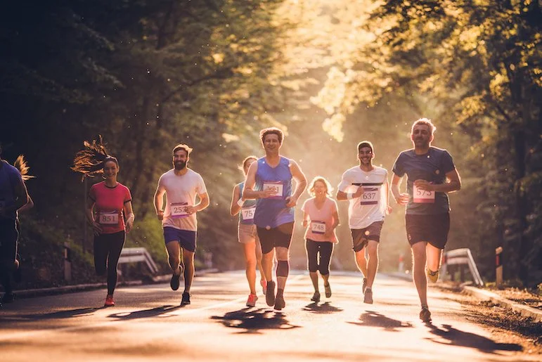 Group of runners participating in a race on a tree-lined road during sunset