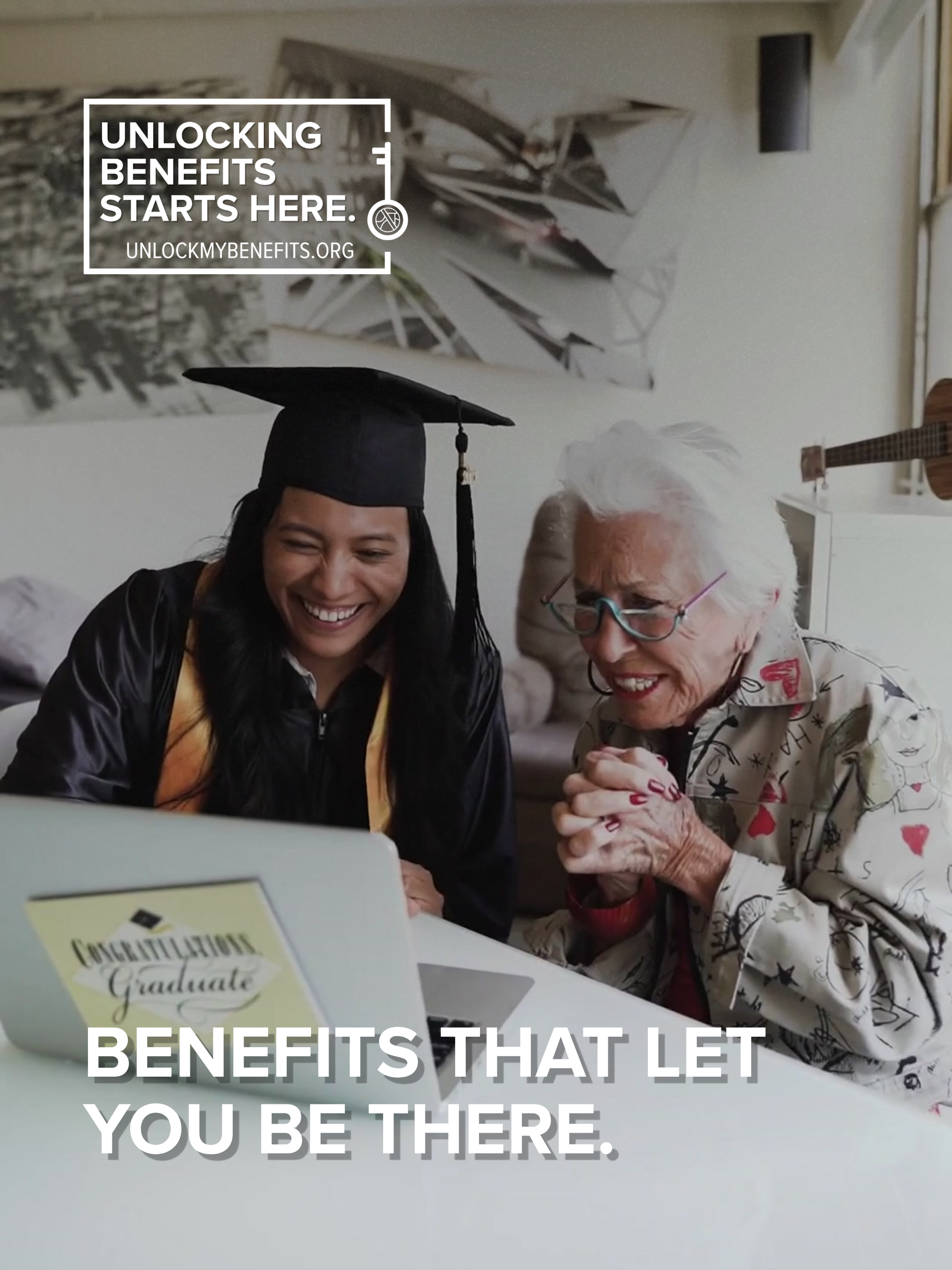 A graduate smiles at a laptop with a congratulatory message. An older woman sits beside, also smiling.