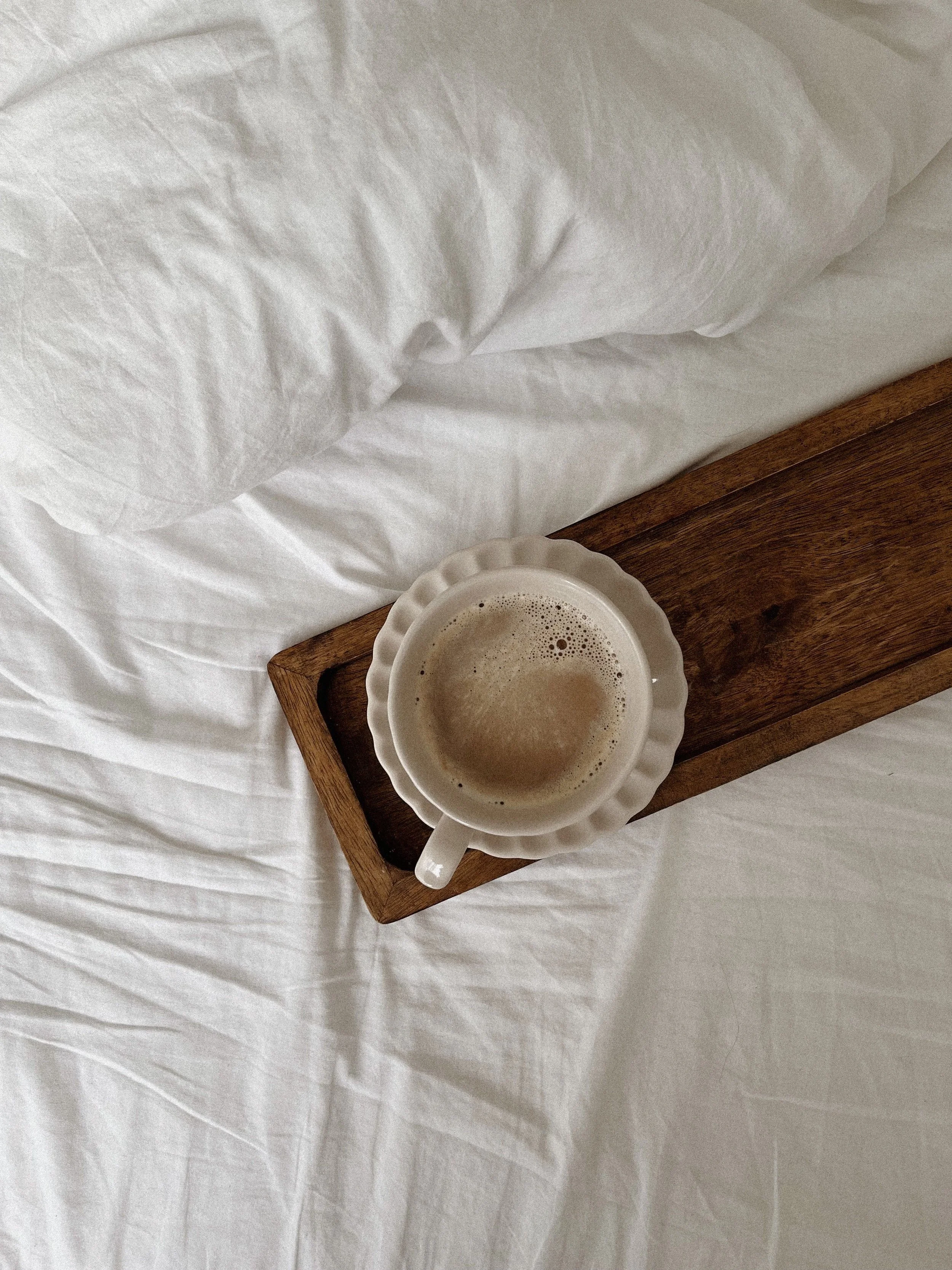 Une tasse de café fumante sur un plateau en bois dans des draps blancs, illustrant le calme, la pause et l'instant présent du monotâche.