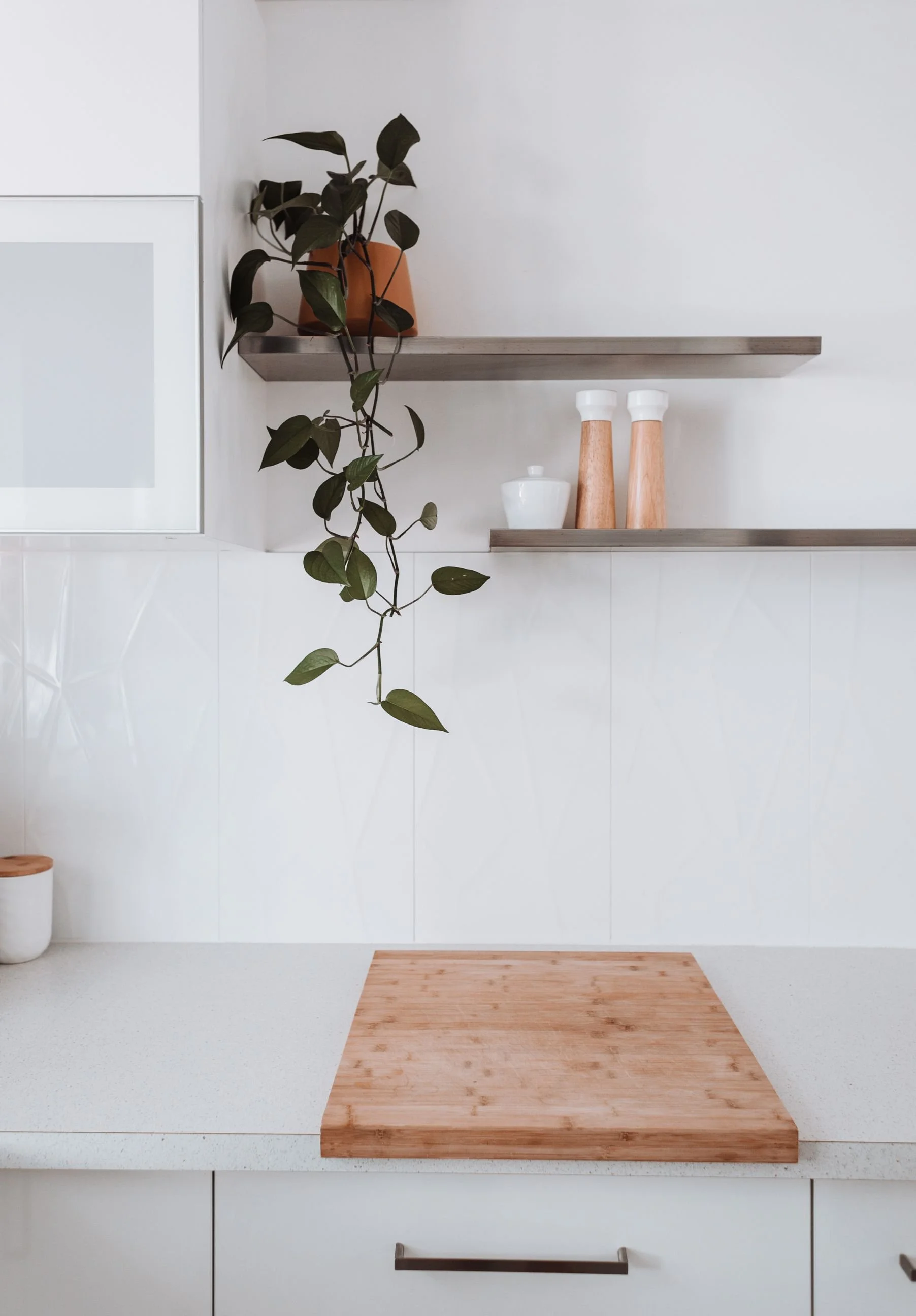 Plan de travail de cuisine blanc, épuré et parfaitement dégagé, avec des étagères murales minimalistes et une plante verte suspendue.