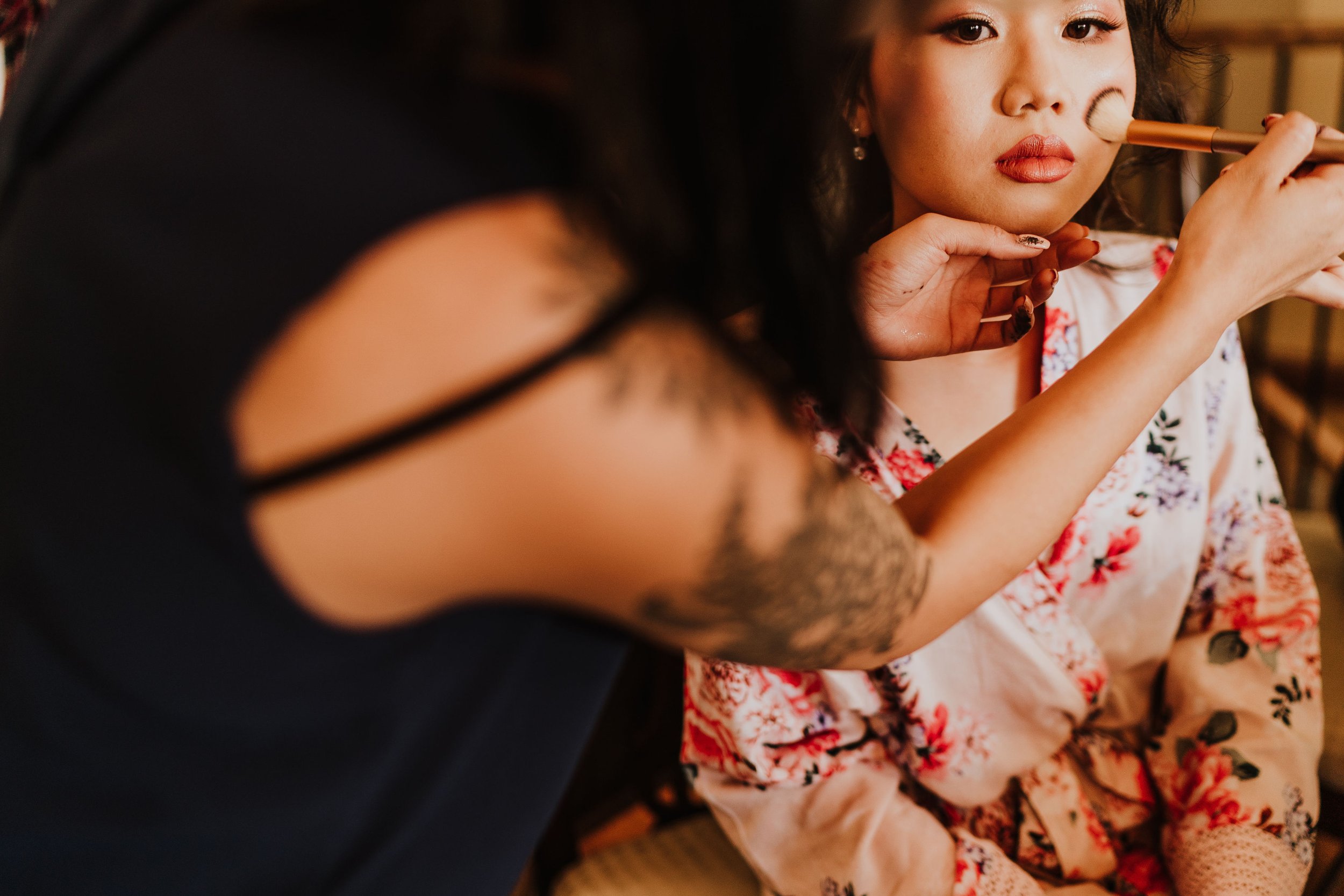 A woman applying makeup to another woman wearing a floral robe.