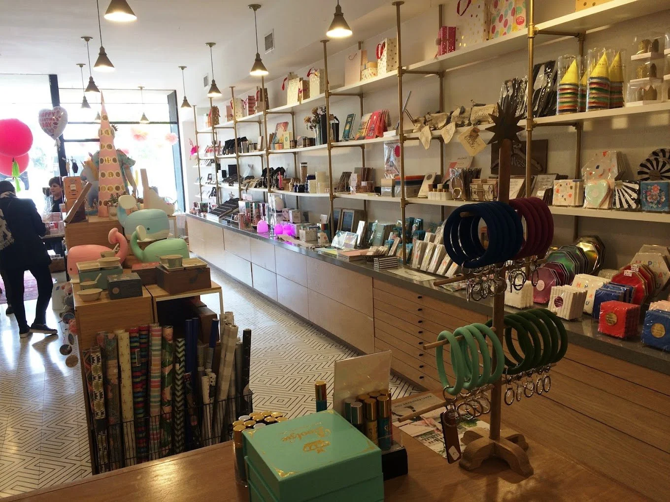 Interior of a gift shop with shelves stocked with various items, colorful balloons, and children shopping.