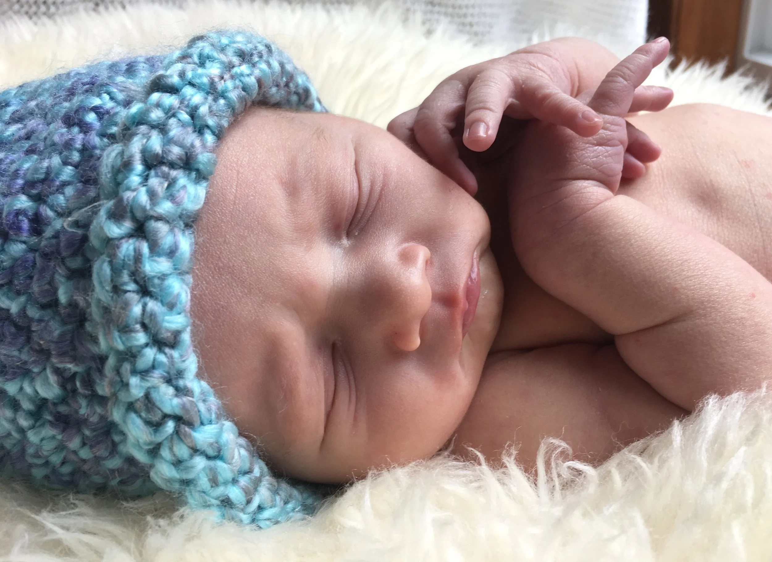 Portrait of a  sleeping baby with a blue crochet hat, nestled on a cream-colored sheepskin rug.