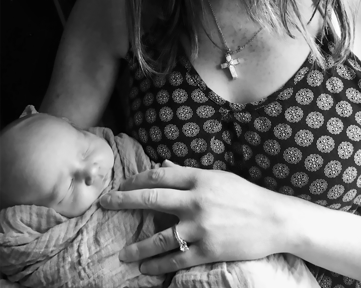 Black and white portrait of a newborn baby swaddled in his mother's arms.