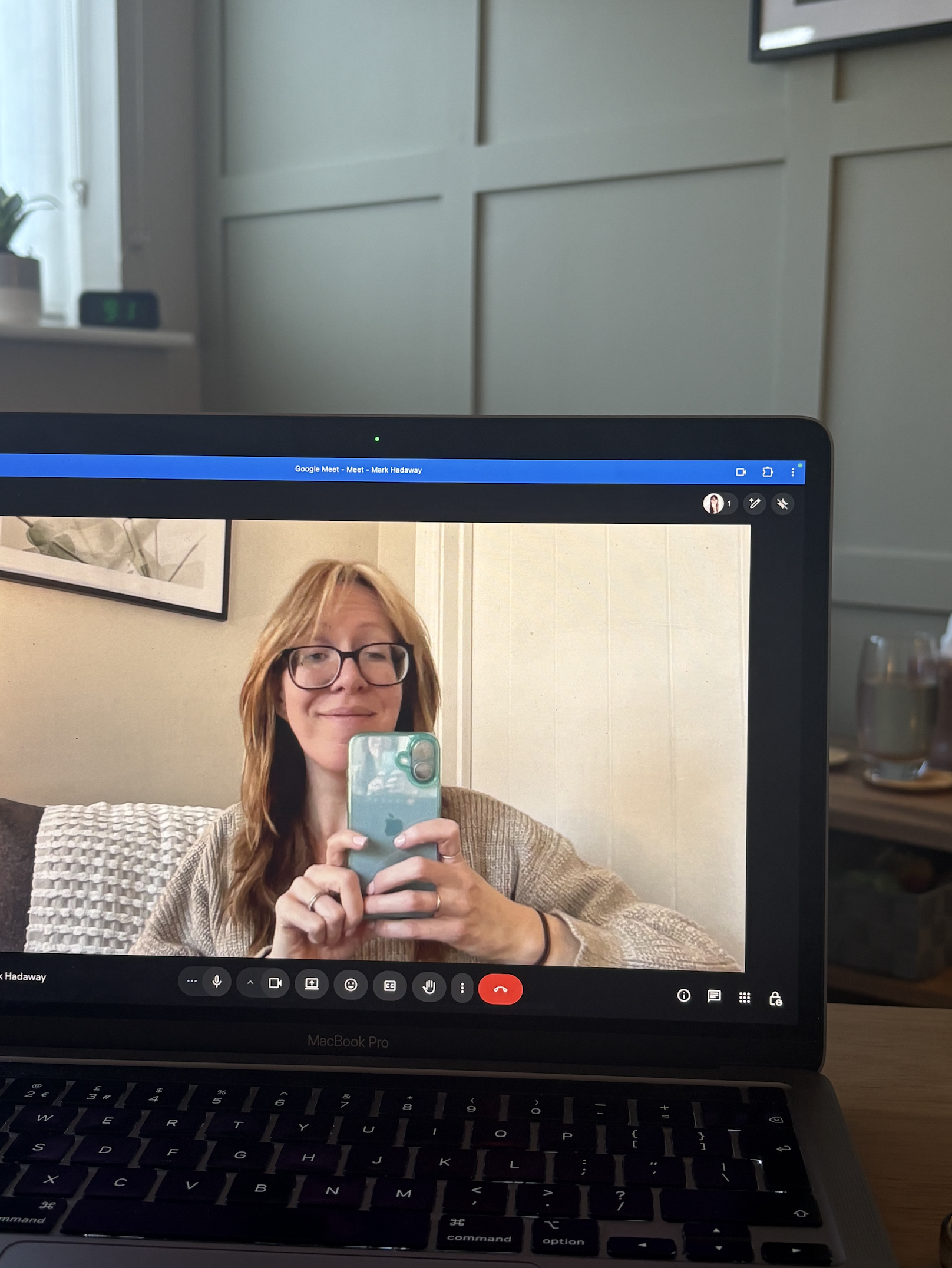 lady sat opposite a laptop taking a selfie with her blue phone