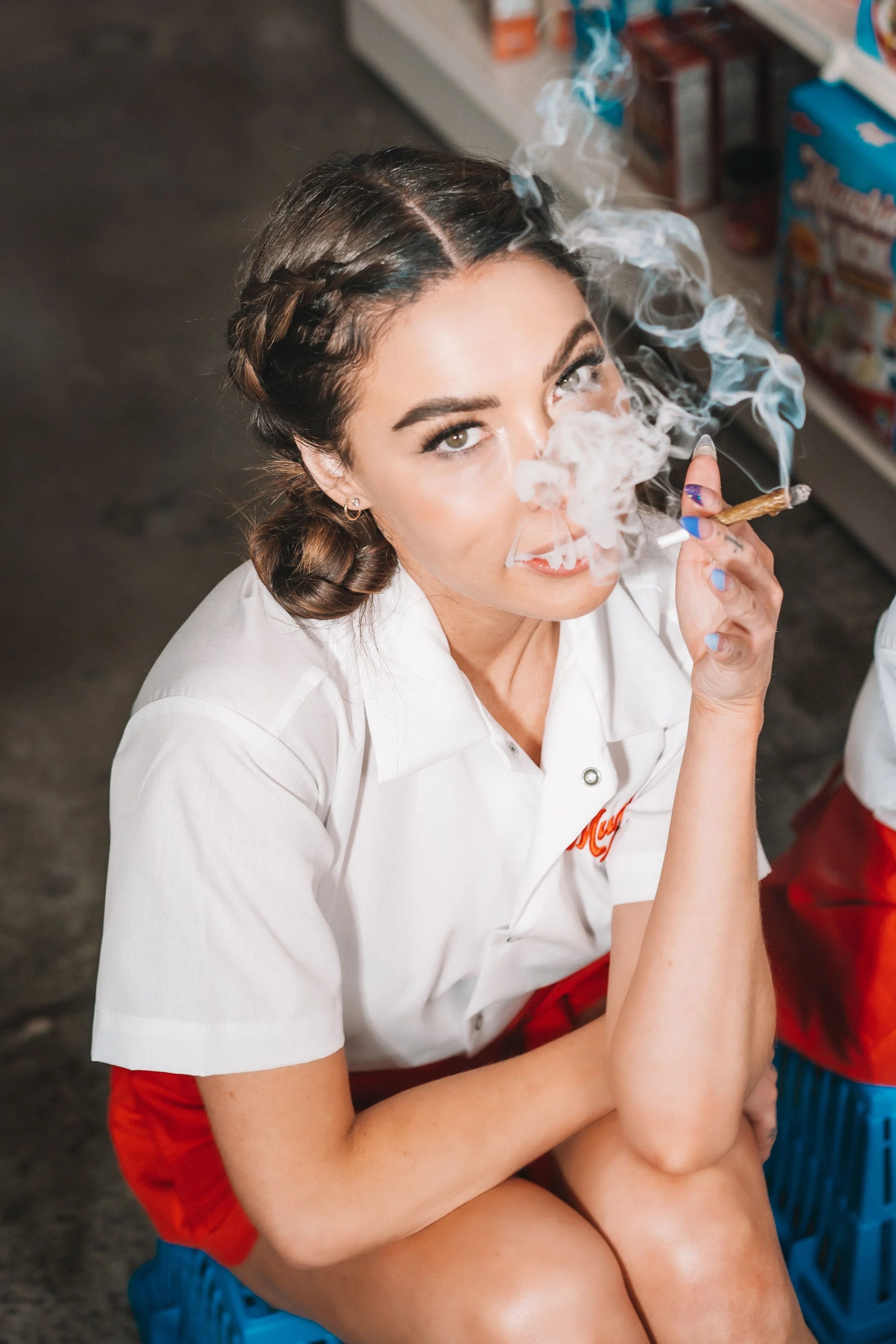 Woman in white shirt and red skirt smoking with smoke visible