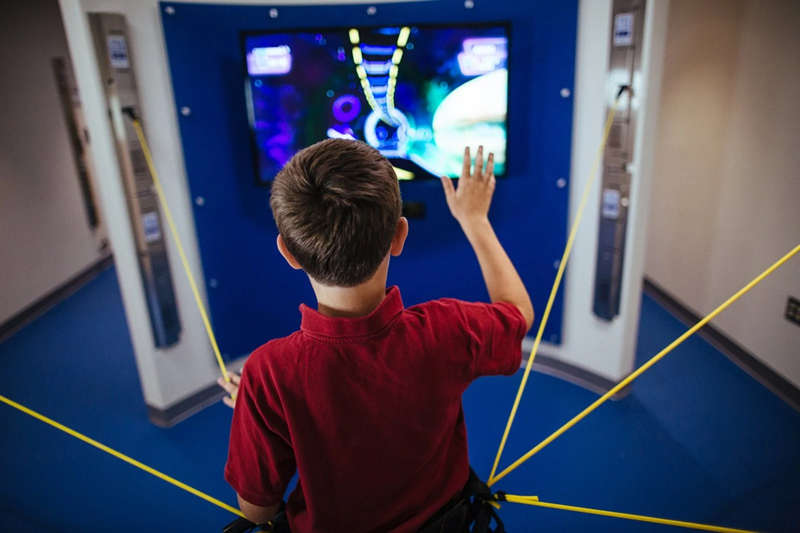 A young boy in a red shirt plays a video game in the integrated pain management clinic